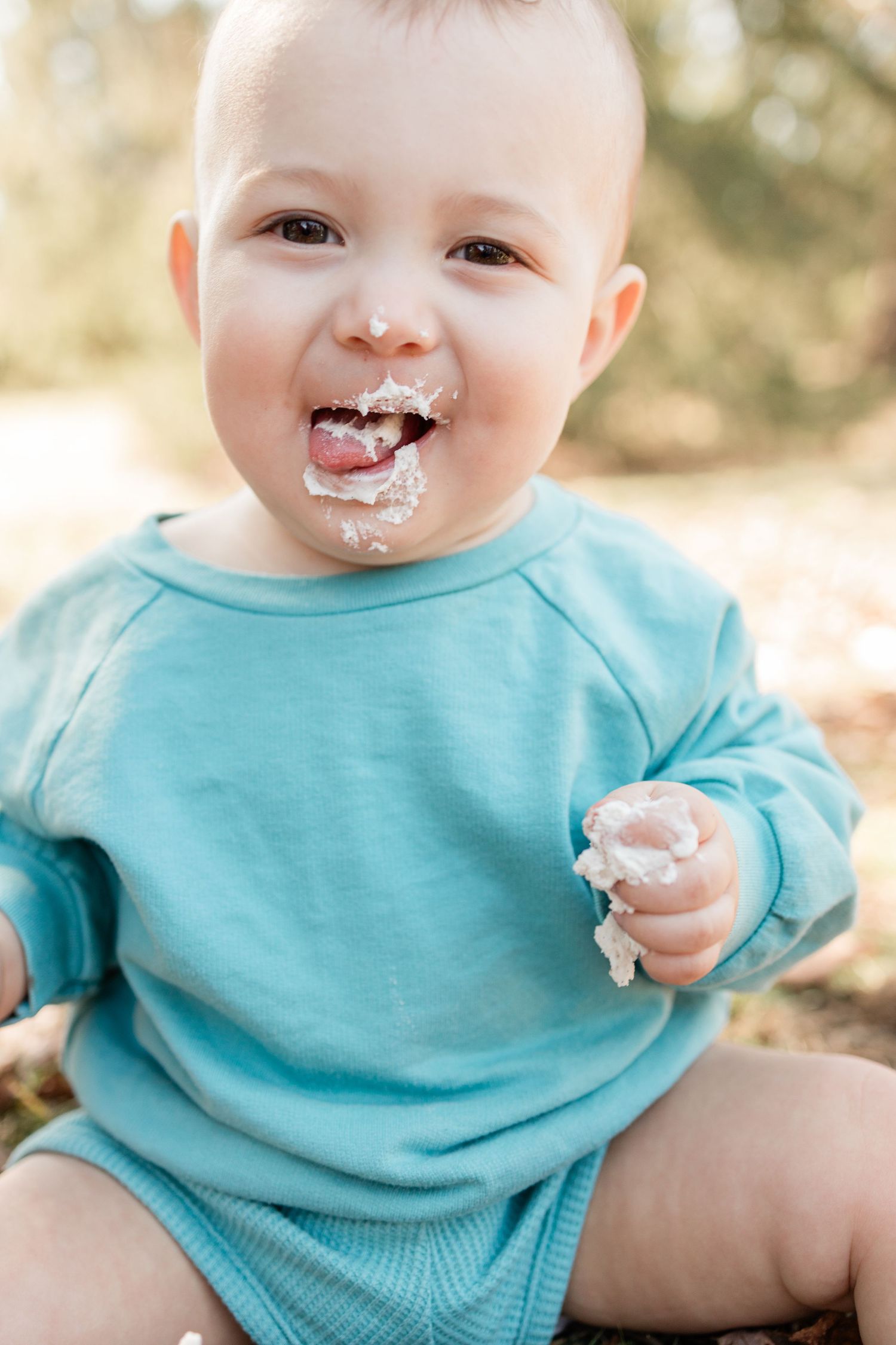 Baby in blue sweatshirt laughing with cake frosting on face.
