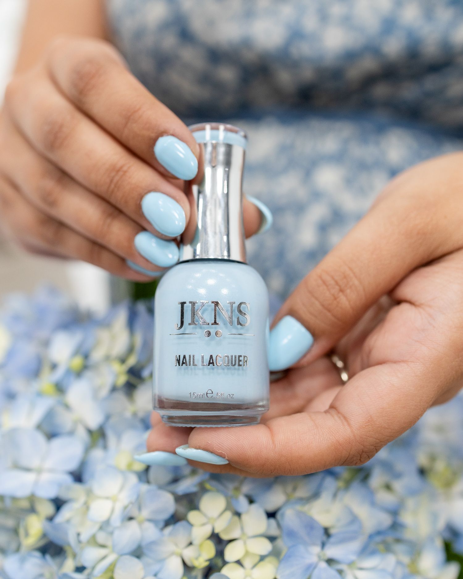 Hands with light blue nail polish holding a bottle of Jacks nail polish against floral fabric.