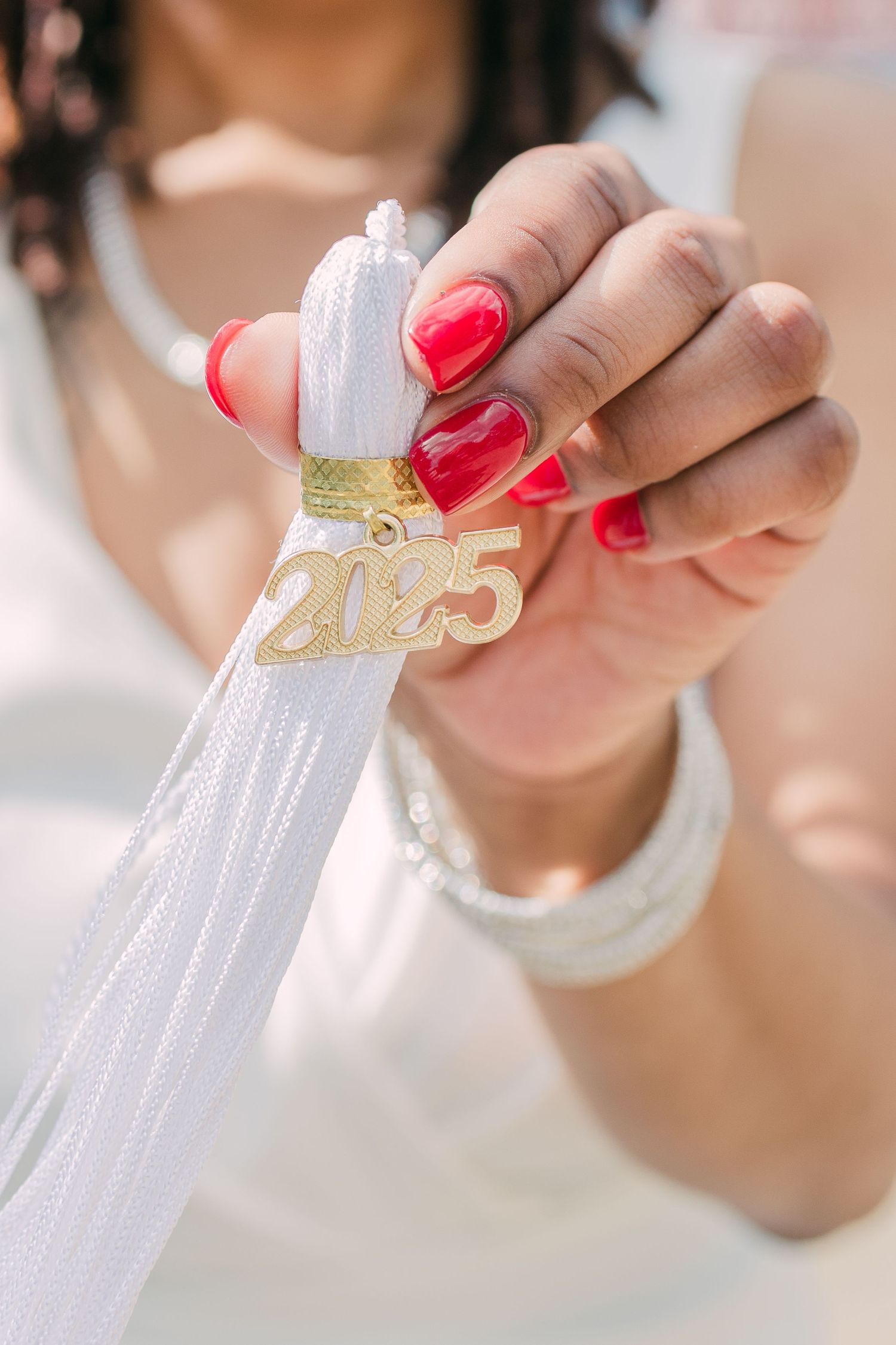 Hand with bright red manicure holding white graduation tassel with gold 2025 charm.