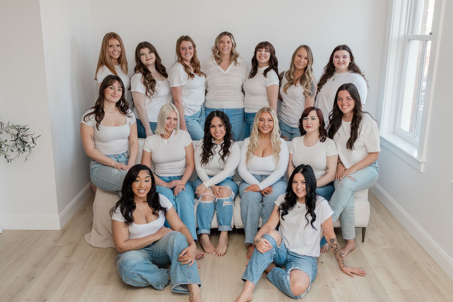 Group photo of women wearing white tops and light denim in bright studio setting.