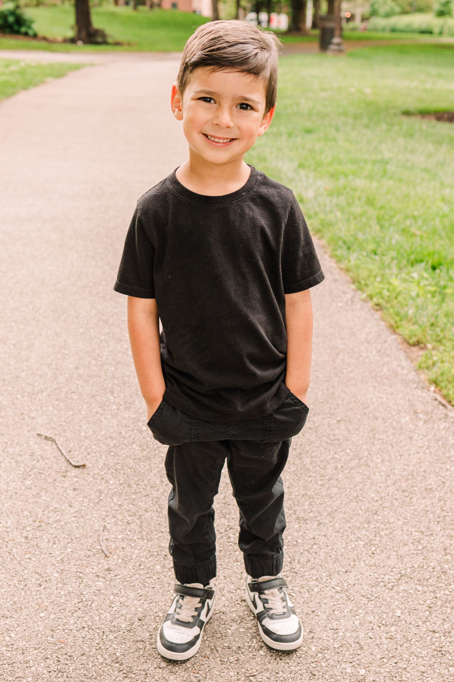 Young person in black t-shirt and pants standing on park pathway.