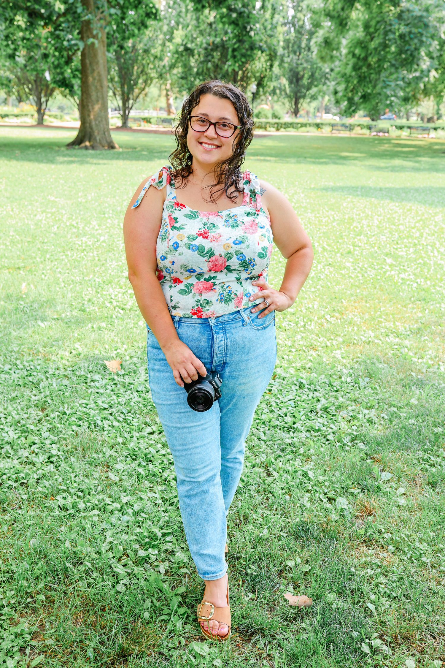 A floral tank top and jeans outfit shown in a green summer park setting.
