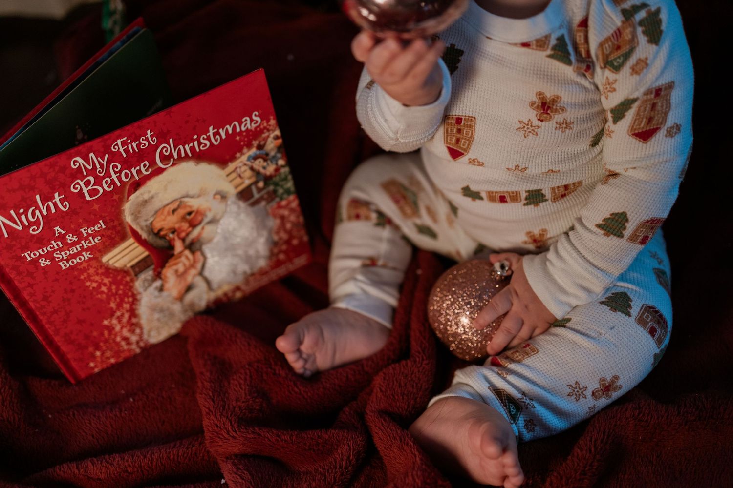 Children in Christmas pajamas read a holiday storybook while gathered on the couch with holiday decor in view.
