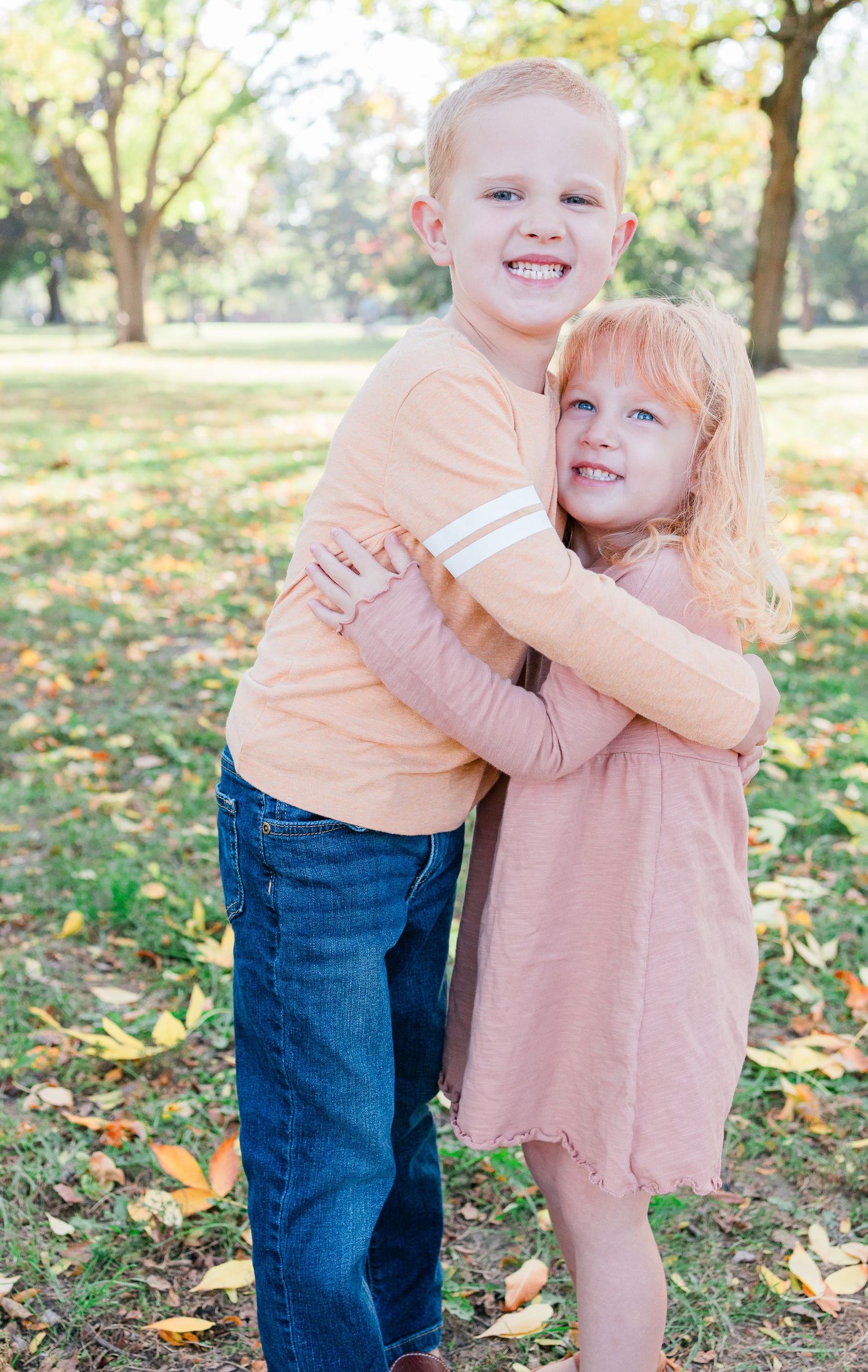 Two children share a joyful embrace while posing outdoors on an autumn day.