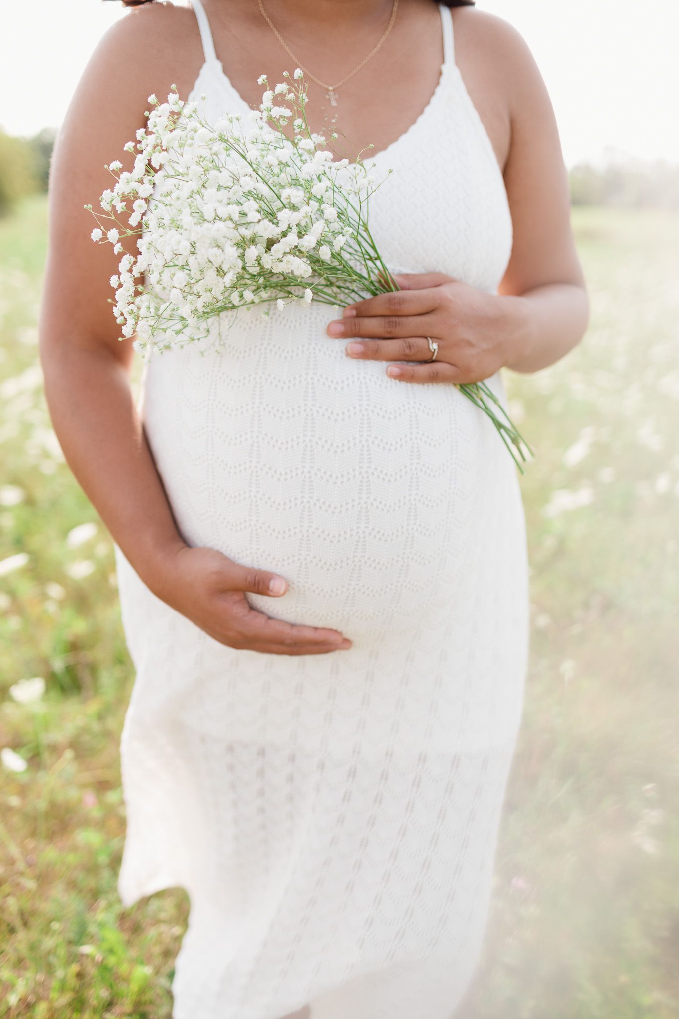 Maternity photo showing white dress and baby's breath flowers in sunlit meadow.
