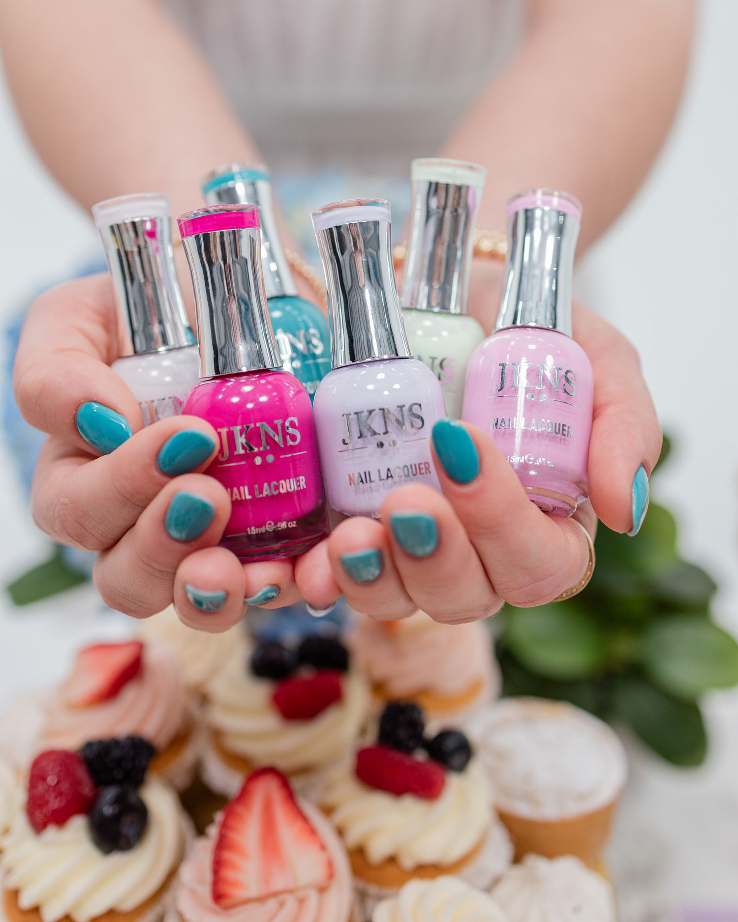 Collection of pink and blue nail polish bottles displayed over mini desserts with fresh berries.