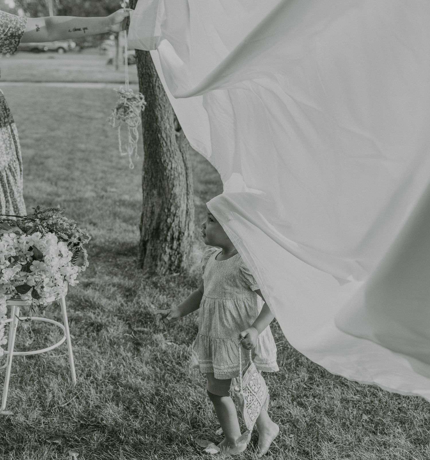 A small child peeks out from behind flowing white fabric during an outdoor photo session.