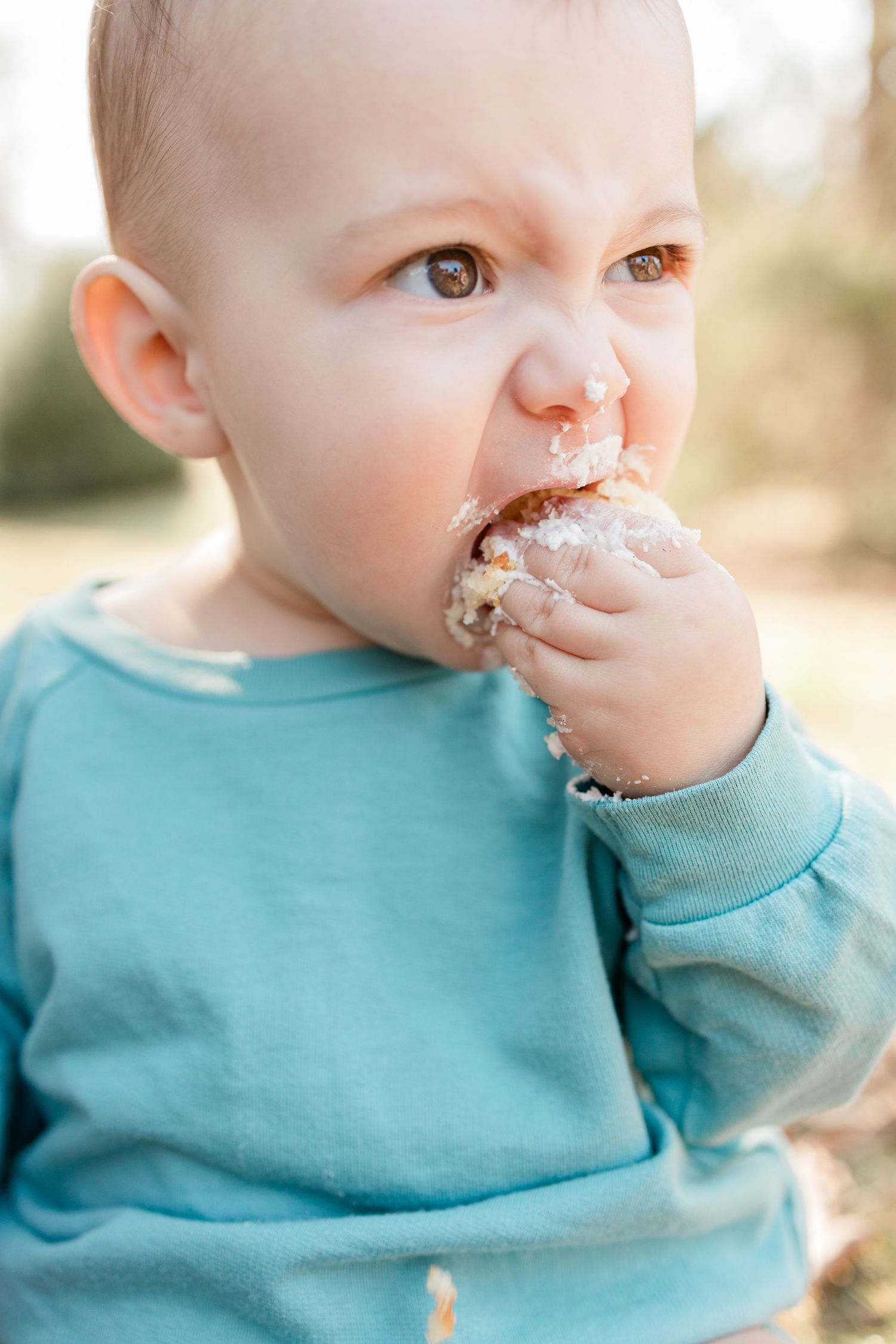 Baby in turquoise sweatshirt enjoying a messy snack outdoors.