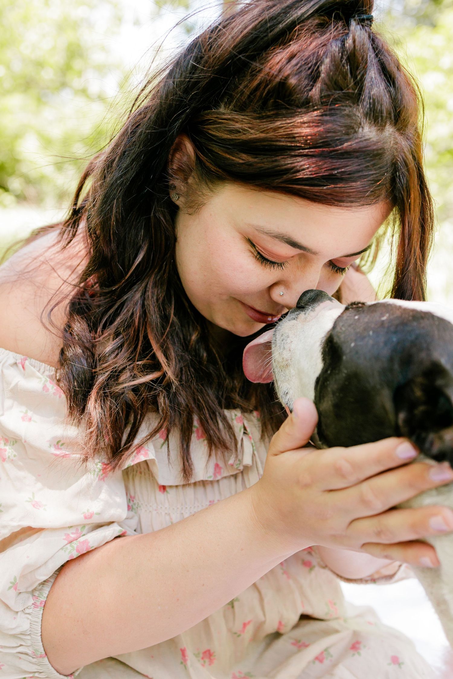 Person in vintage dress shares tender moment with black and white dog outdoors.