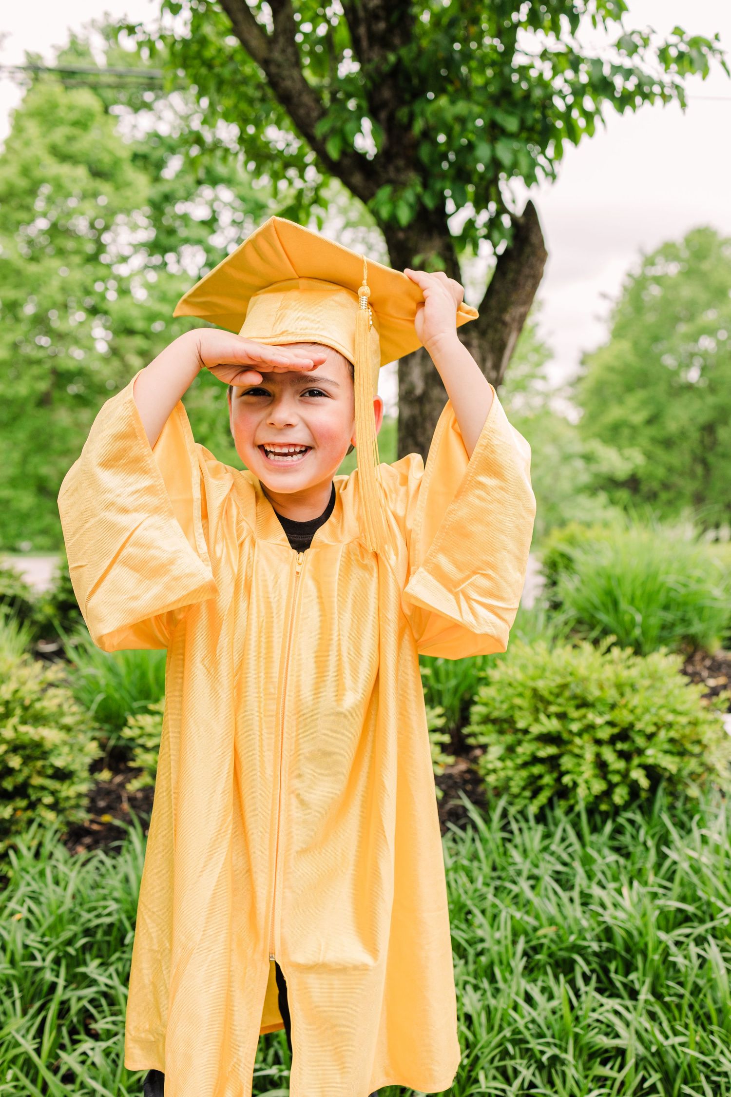 Graduate in bright yellow cap and gown playing with their mortarboard outdoors.