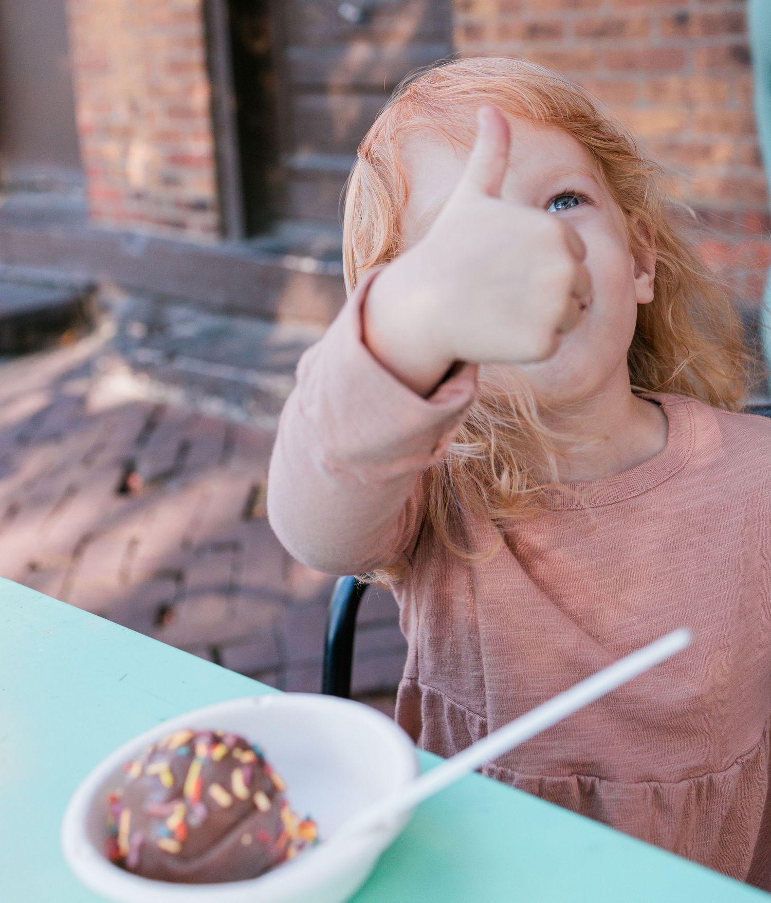 A child in pink makes a silly face while eating dessert at a turquoise table.