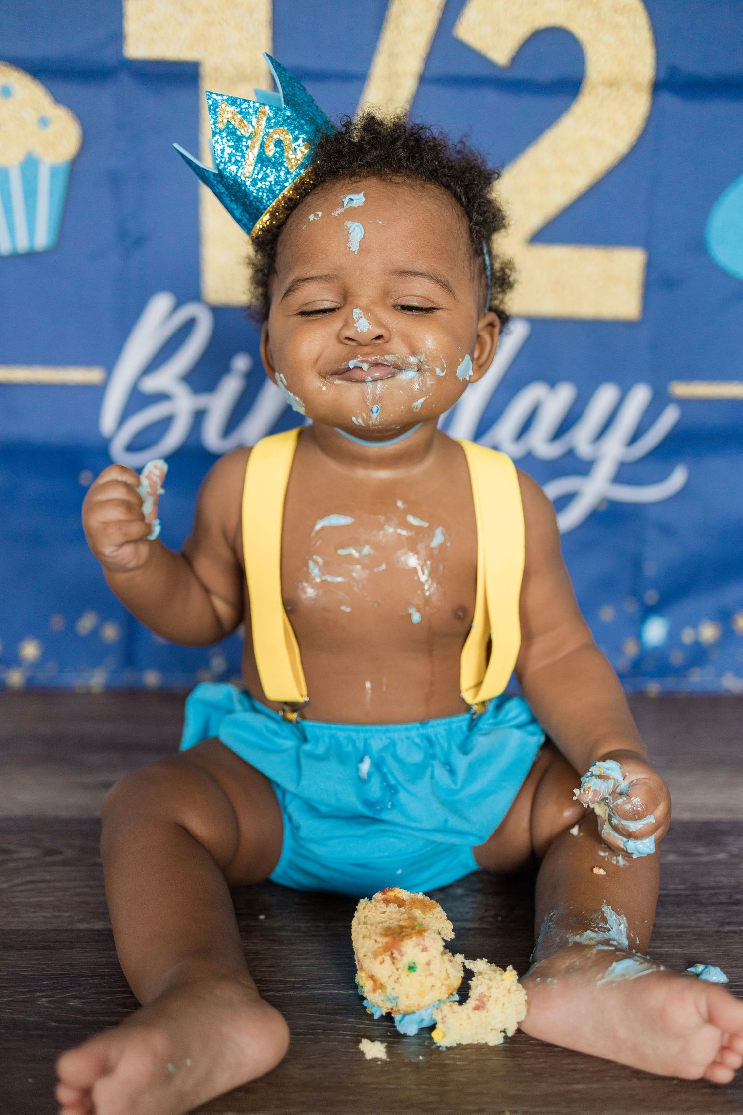 Messy cake smash photoshoot with blue and yellow decorations against dark wood flooring.