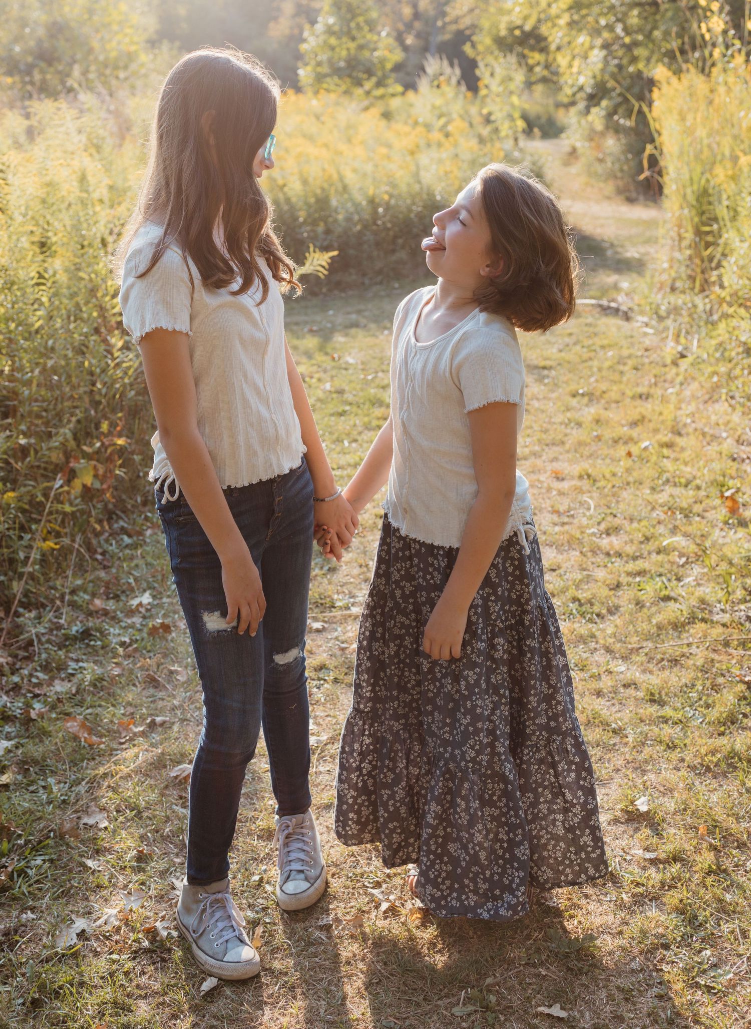 Two young people in casual attire share a playful moment on a sunlit nature path.