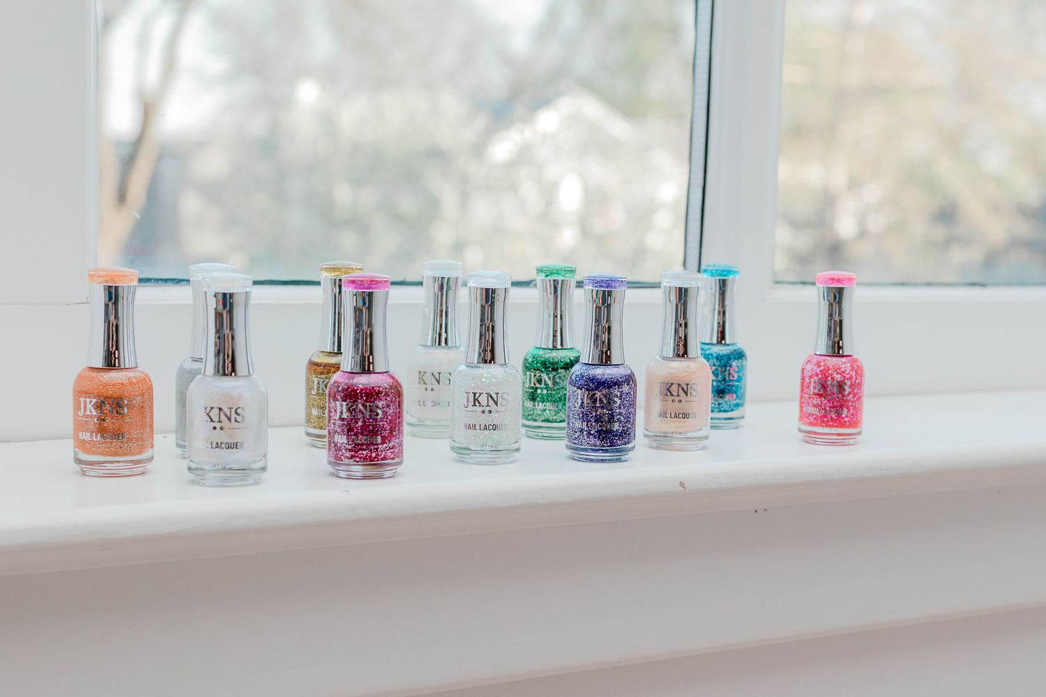 Colorful nail polish bottles lined up on a white windowsill in natural light.