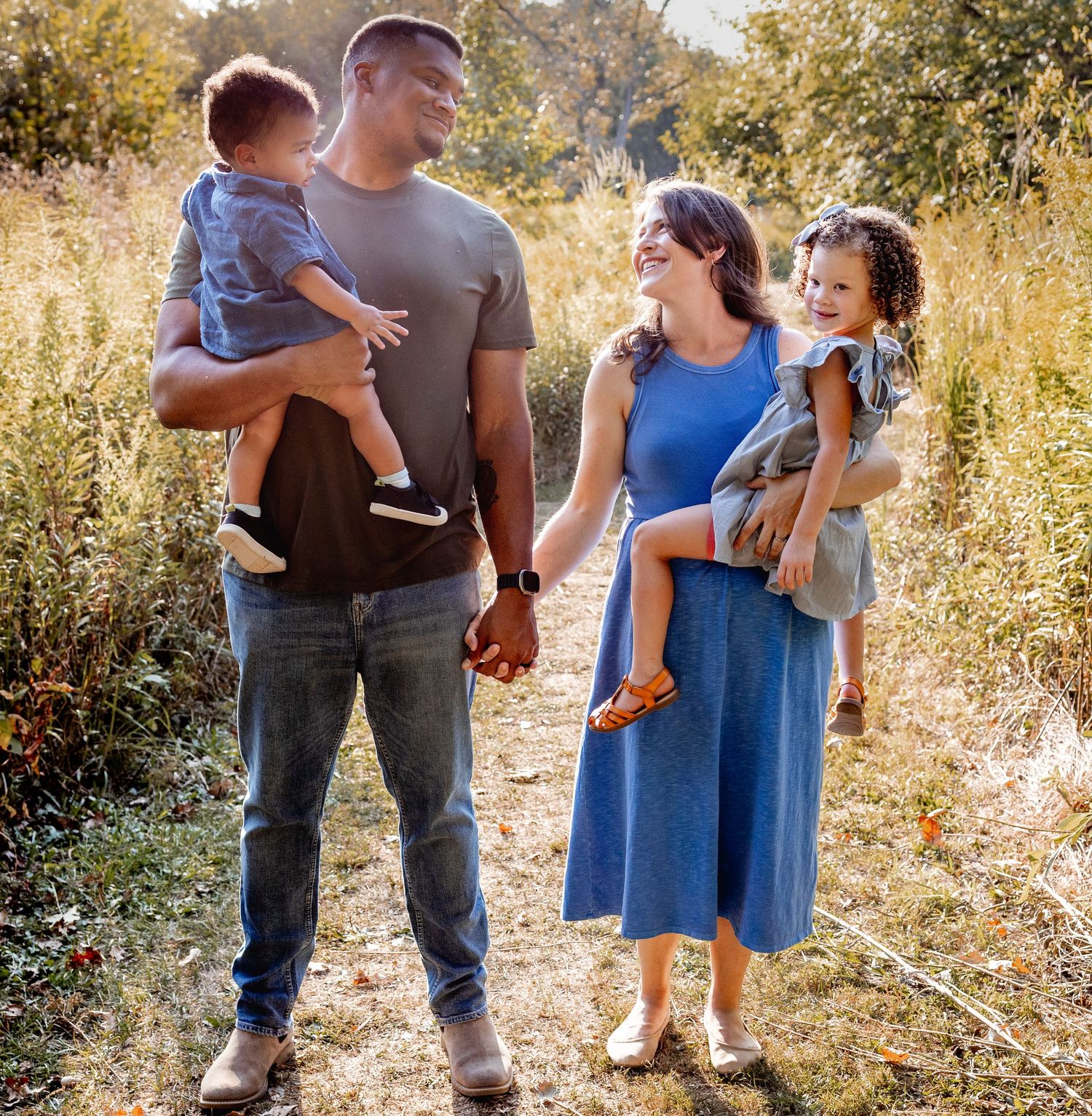 Family of four posing together outdoors on a nature trail in warm evening light.
