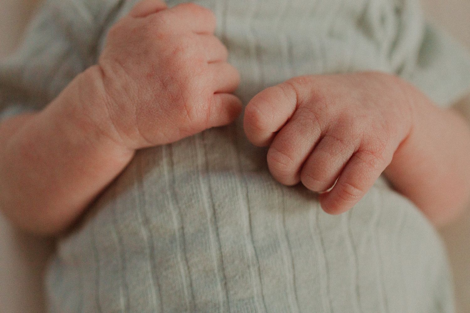 Close-up view of tiny baby hands resting on soft gray fabric with gentle natural lighting.