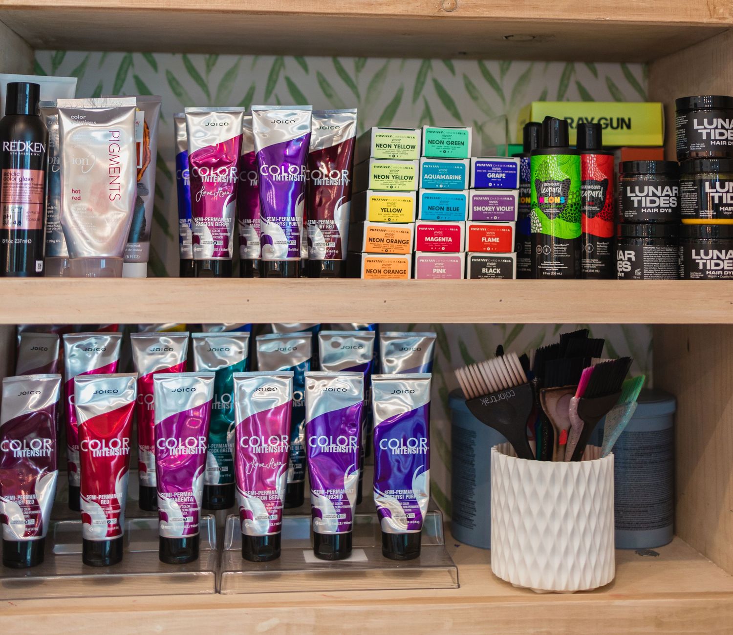 Hair dye products and styling tools organized on wooden shelves in a salon setting.