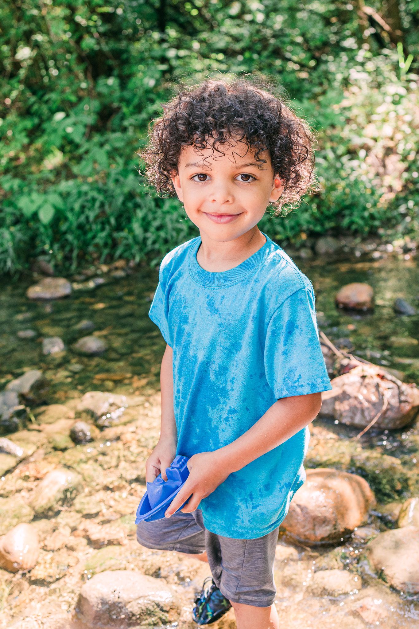 Child in bright blue t-shirt and shorts playing by a rocky stream on a sunny summer day.