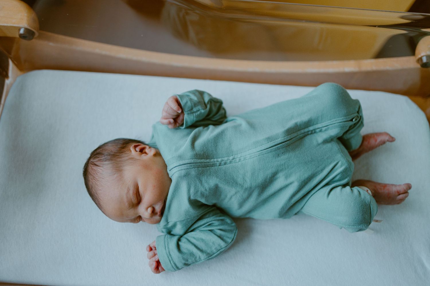 A baby in mint green onesie pajamas crawling and rolling on white bedding from left to right in progressive stages.