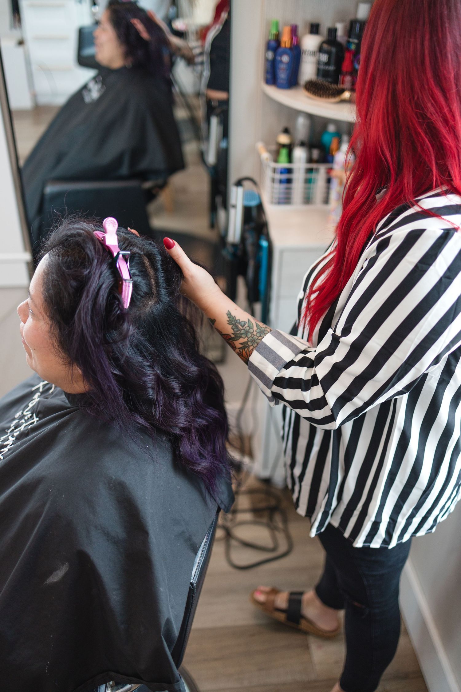 Hair stylist with striped shirt styling purple-tinted hair in a salon setting.