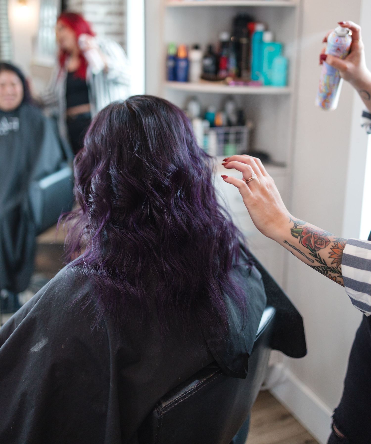 Hair stylist applying product to client's purple-tinted hair in professional salon chair.