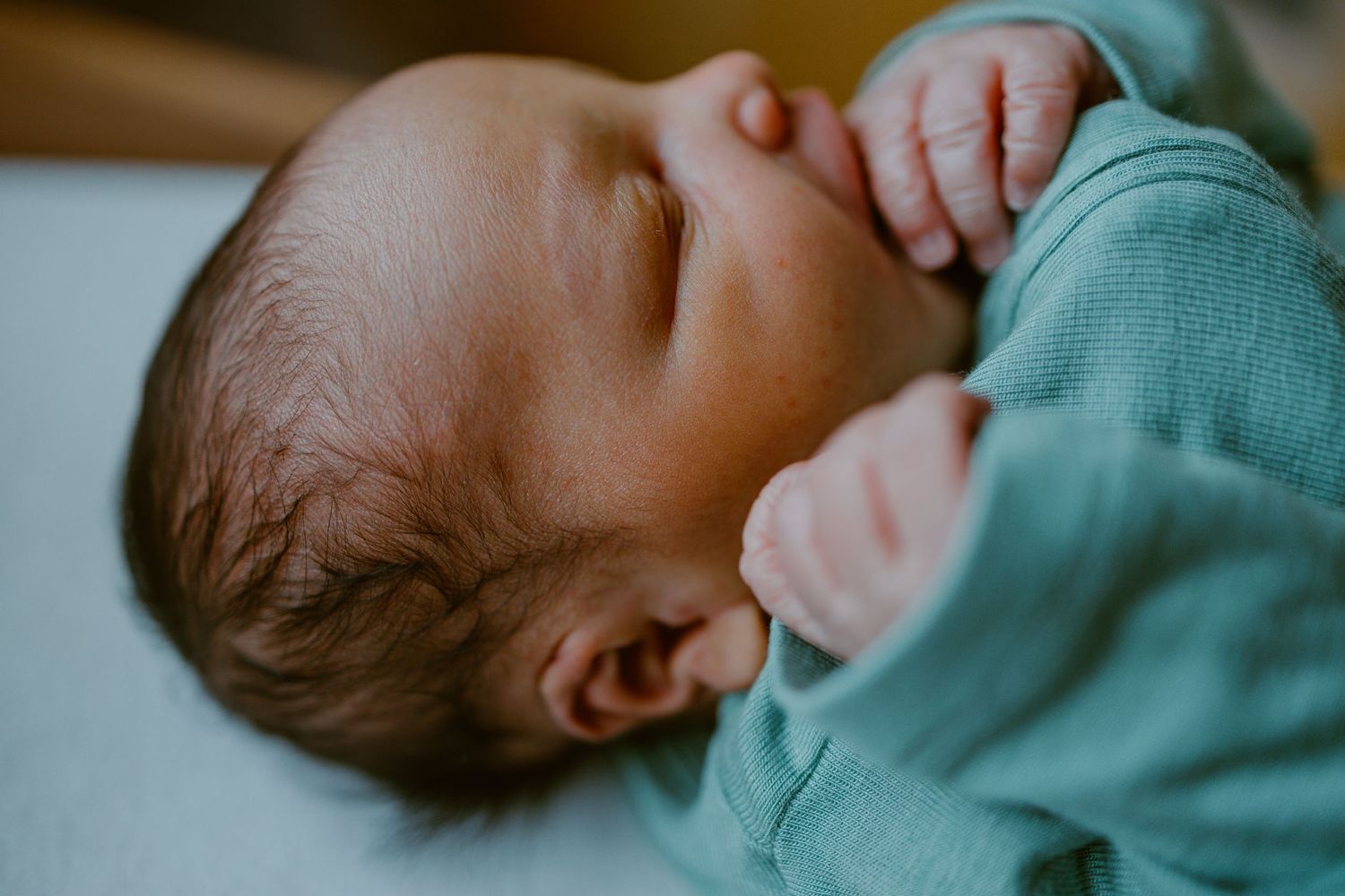 A baby in a turquoise bodysuit lies sleeping on a white sheet in a side-by-side photo sequence.