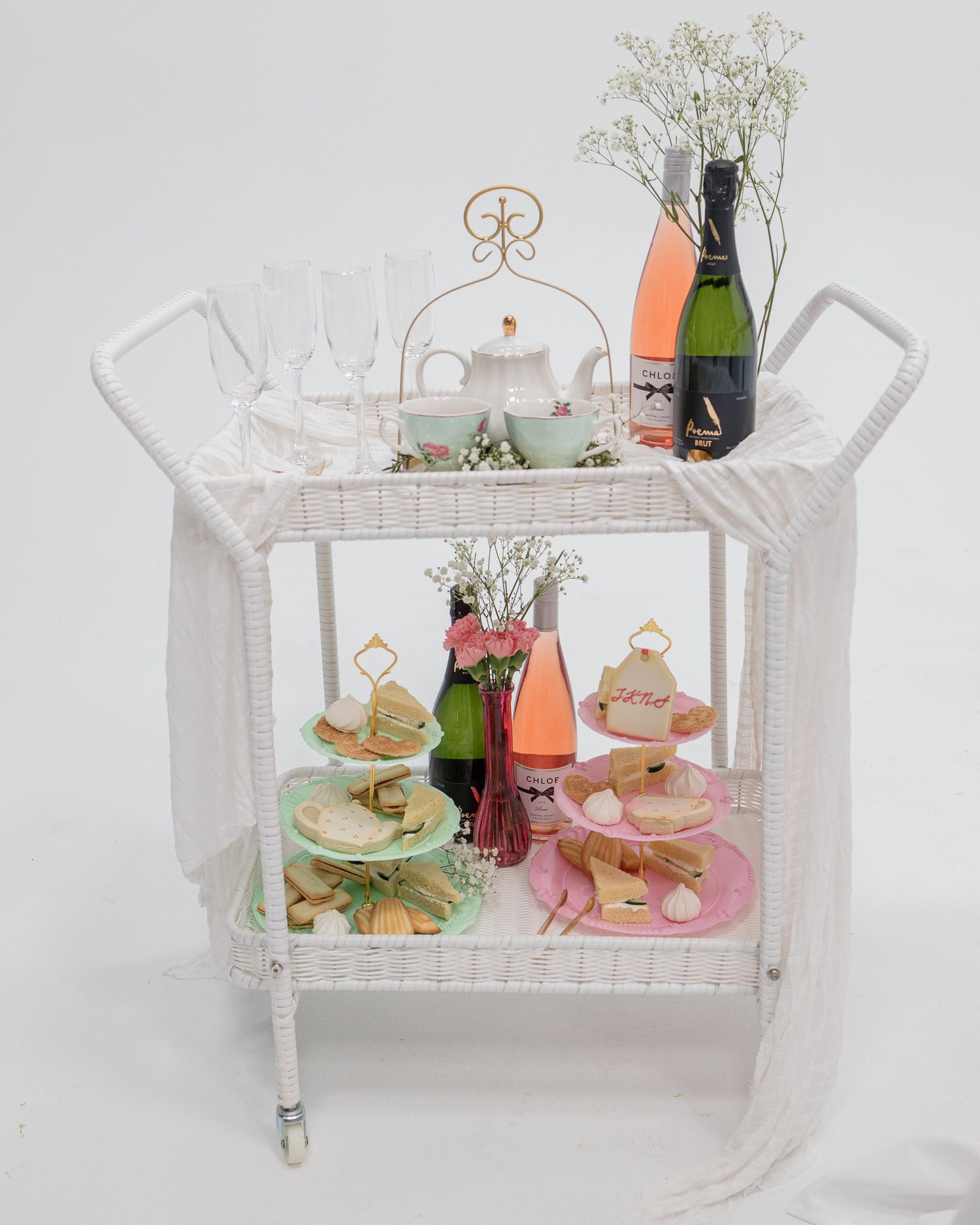 Elegant white tea cart with champagne, tiered dessert stands, and delicate glassware.