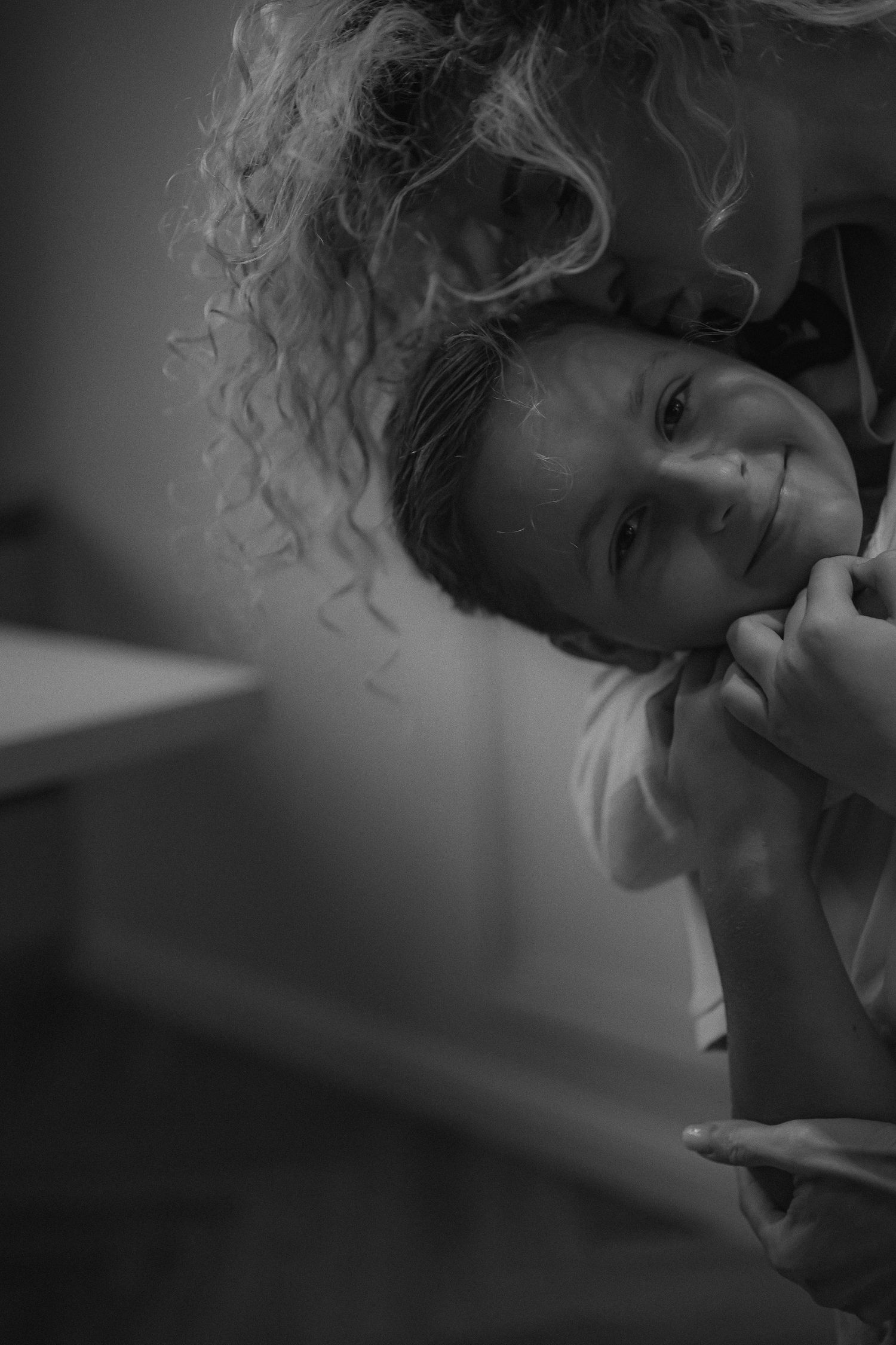 Black and white photo of a smiling child being hugged by a curly-haired person in a tender moment.