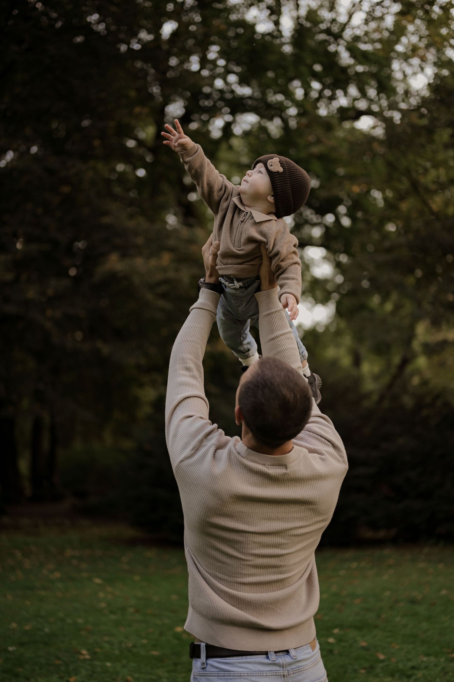 A father lifting his young child high in the air while playing outdoors in a green park.
