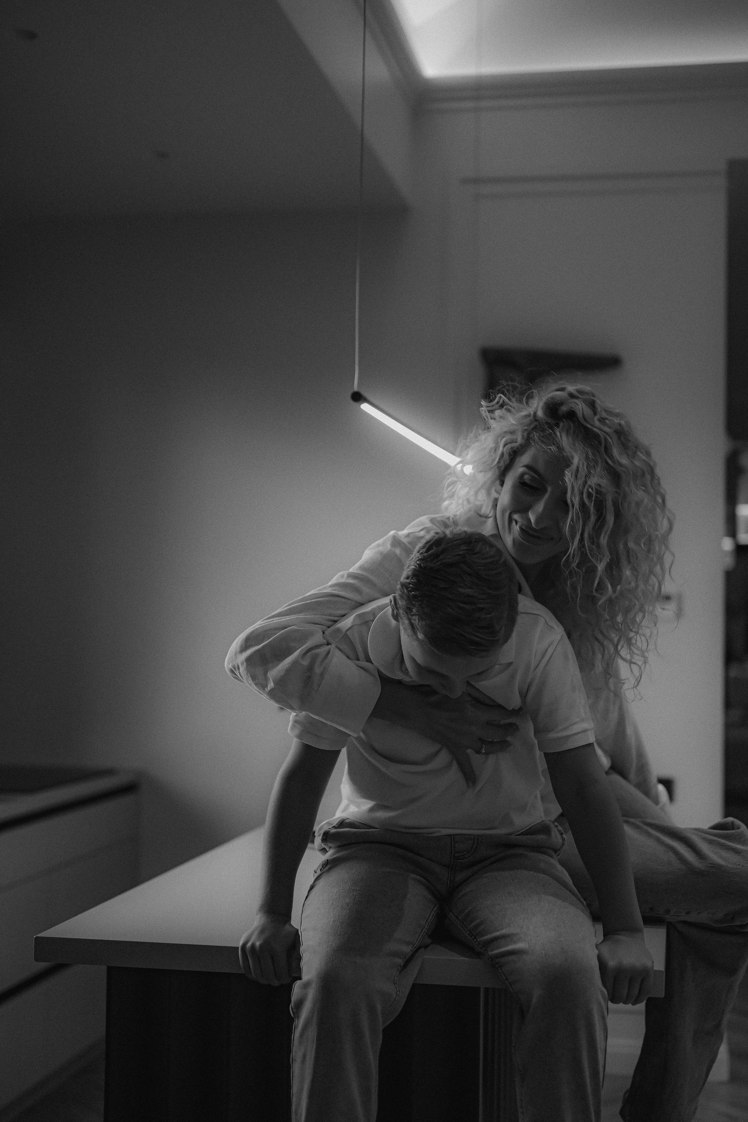 Black and white photo of a couple sharing an intimate moment under a pendant light.