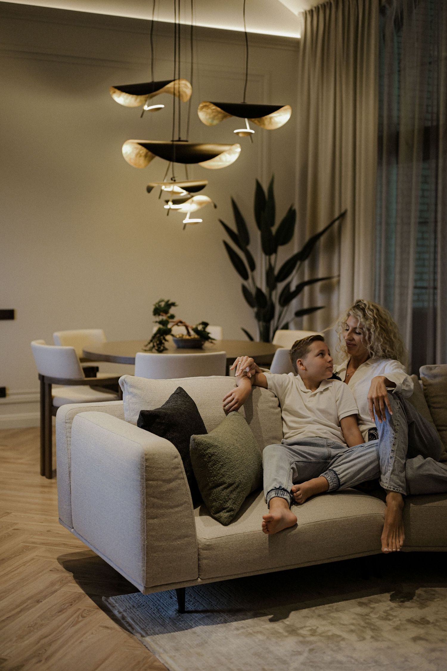 Couple relaxing on a beige sofa under elegant pendant lights in a modern living room.