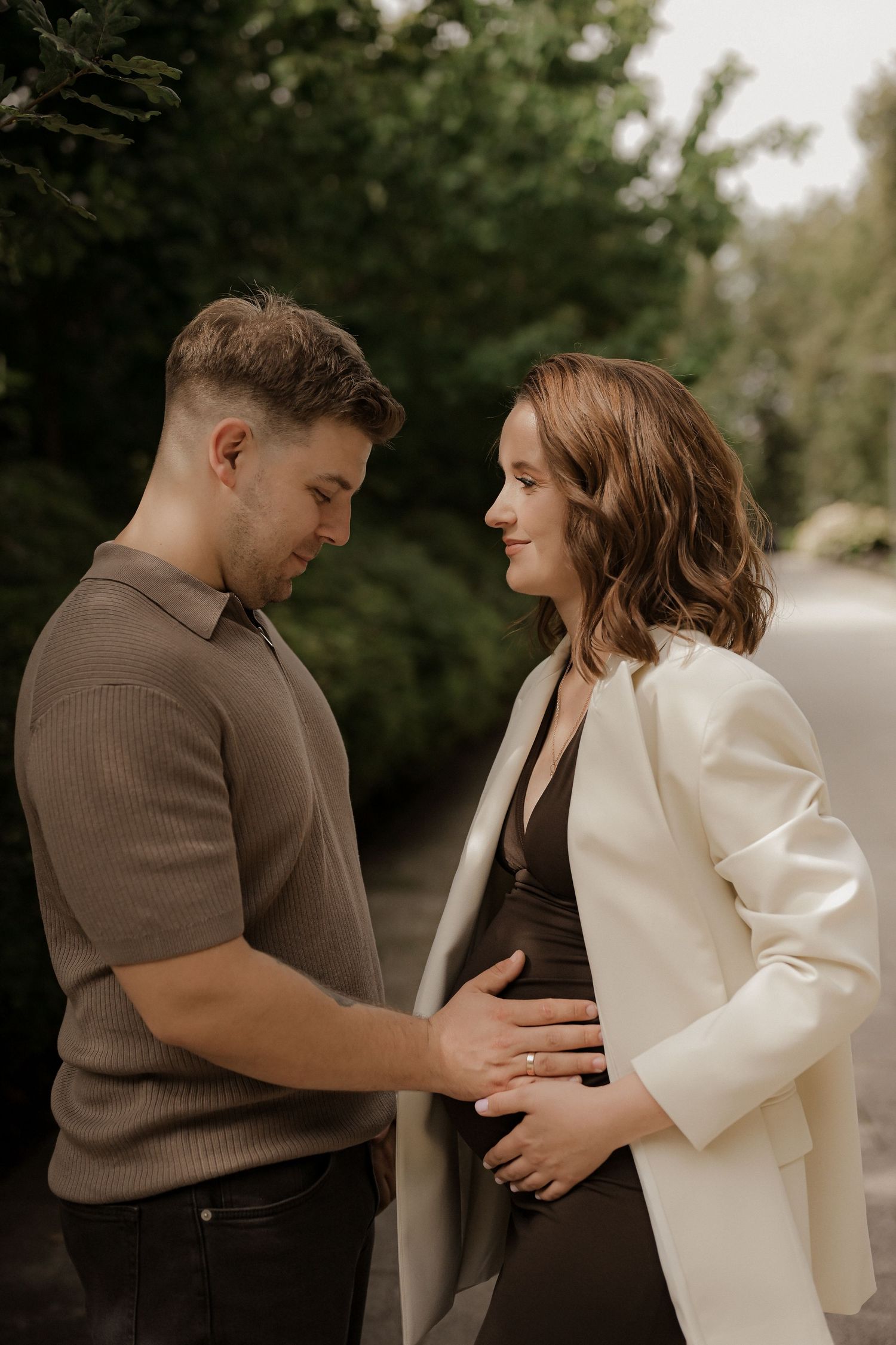 A couple shares a tender moment outdoors, with the man gently touching the womans baby bump during a maternity photo session.