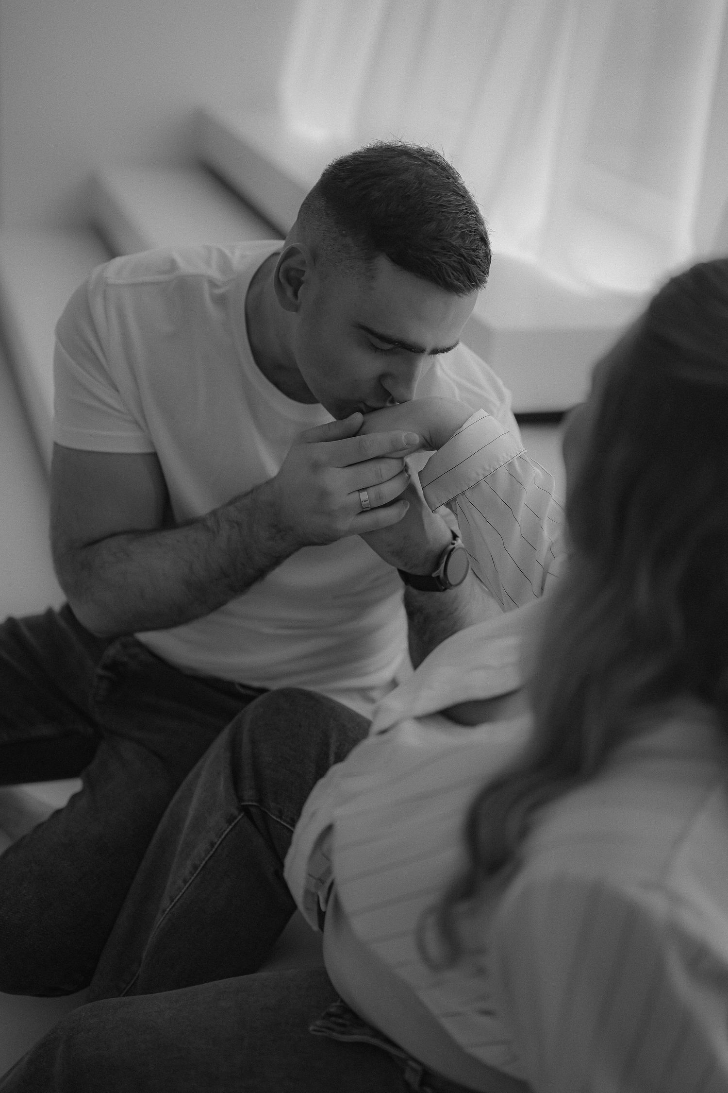 Black and white photo of a man kissing a woman's hand while sitting together indoors.