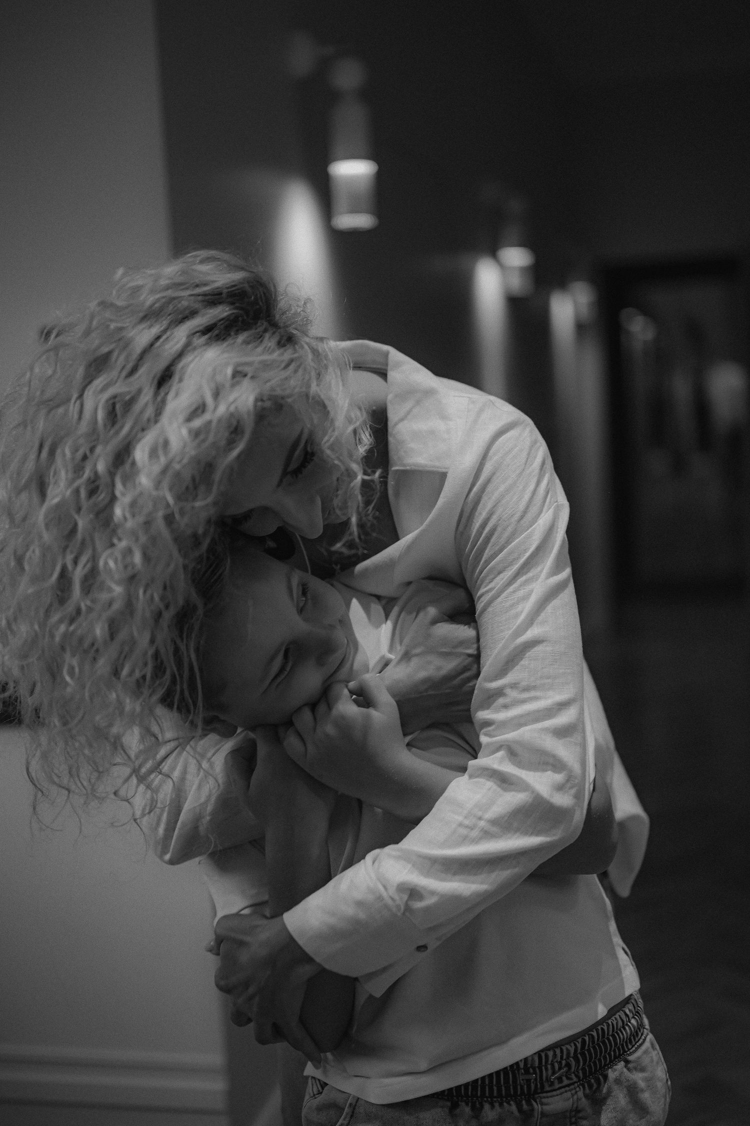 A woman with curly hair embraces a young child in a tender black and white photo.