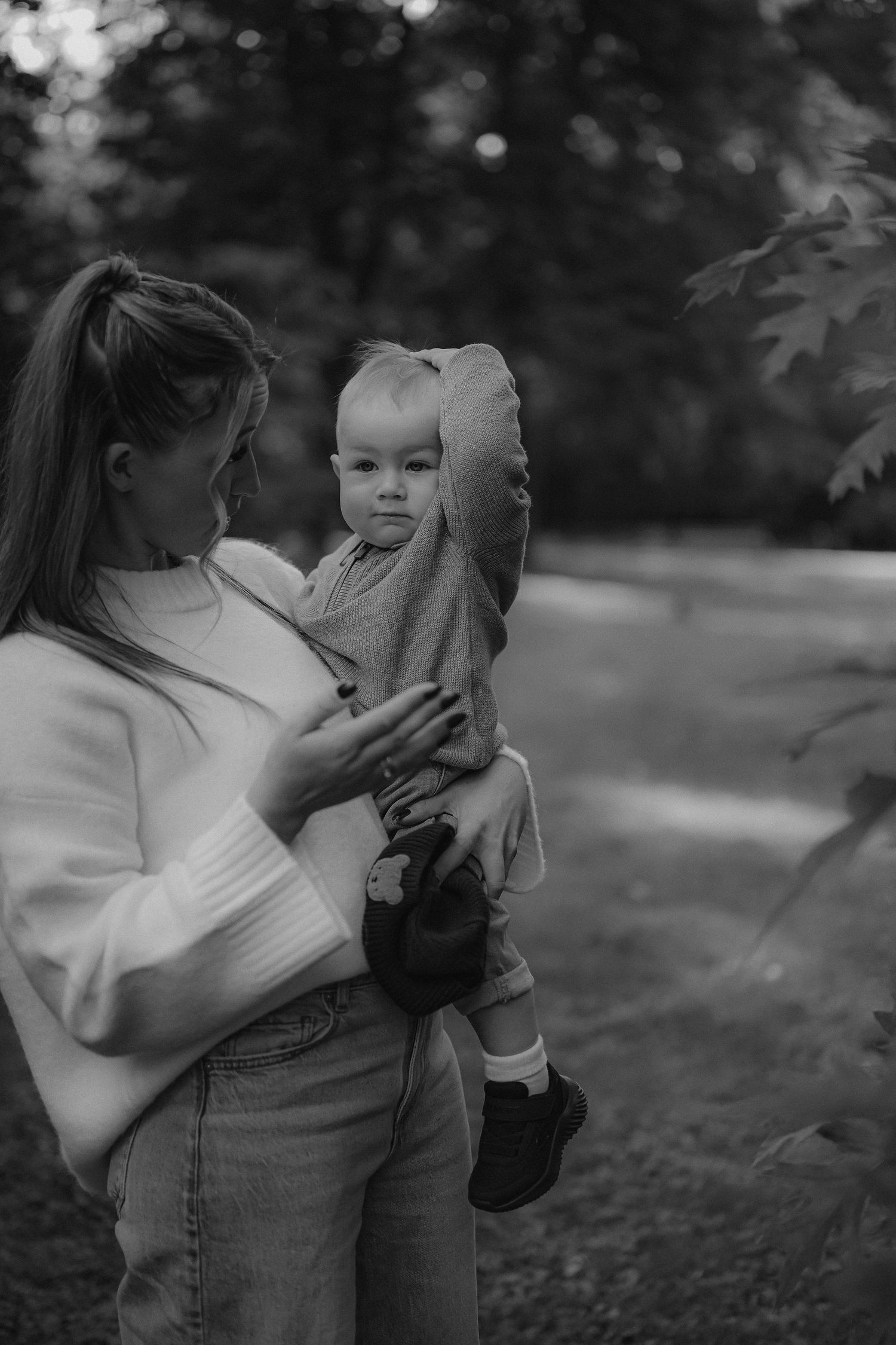 Black and white photo of a young mother holding her baby outdoors in a park setting.