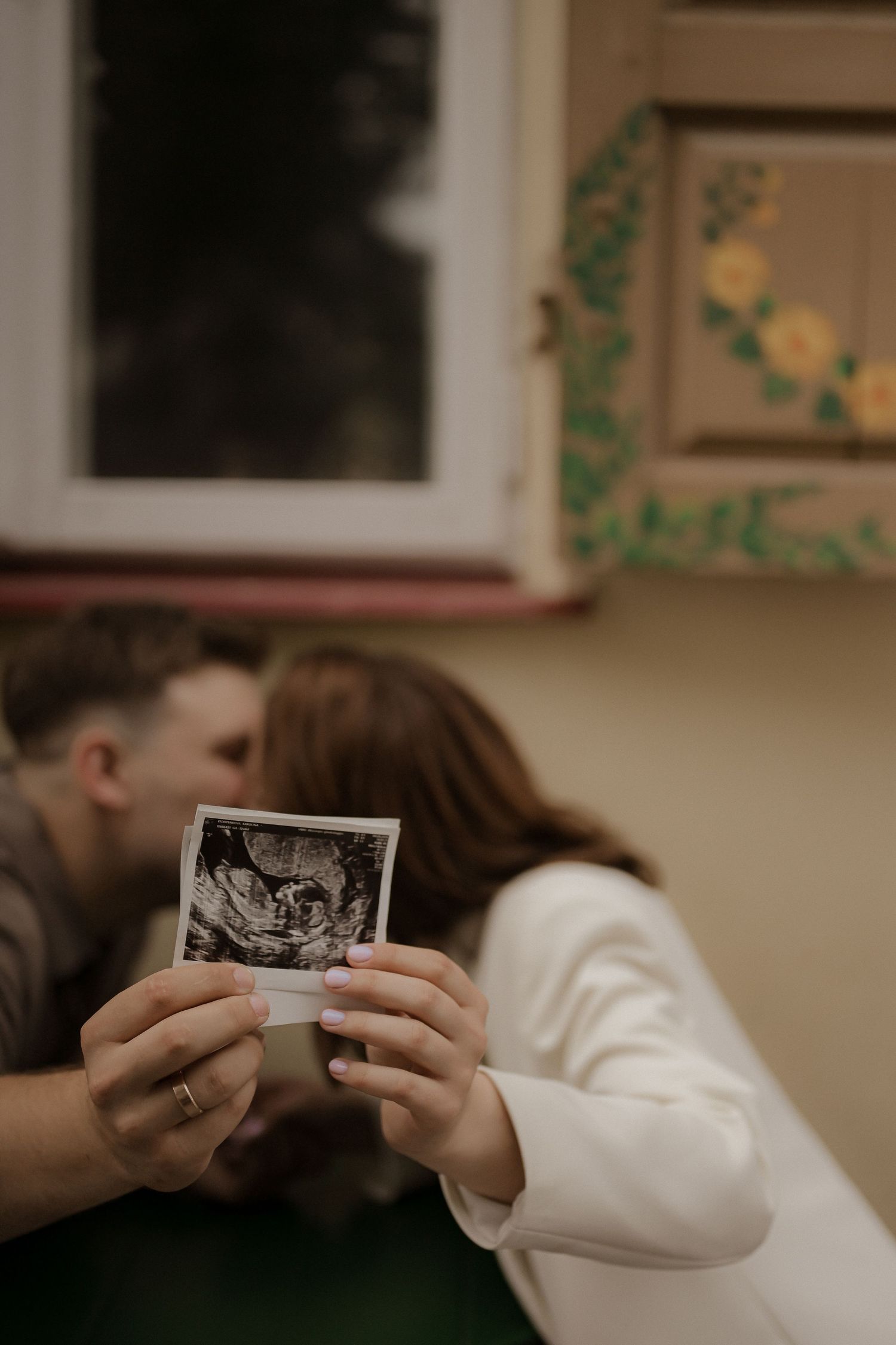 Couple kissing while holding an ultrasound photo, announcing pregnancy in a cozy home setting.
