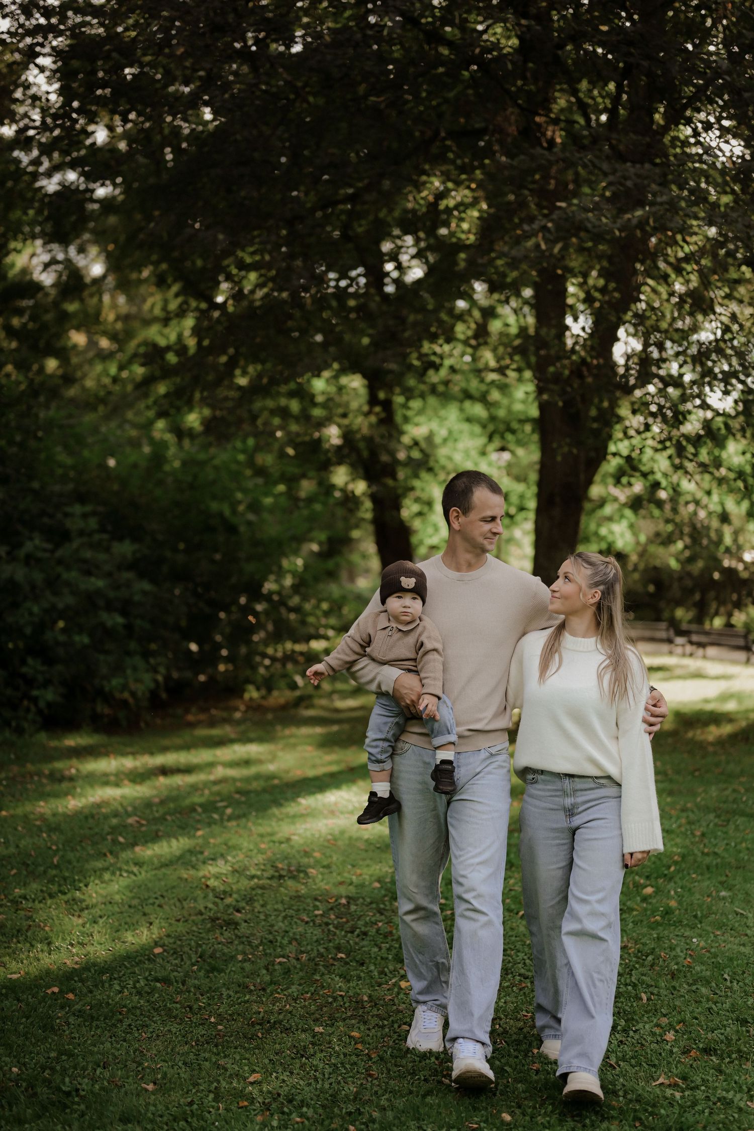 Happy young family with baby walking in a lush green park on a sunny day.