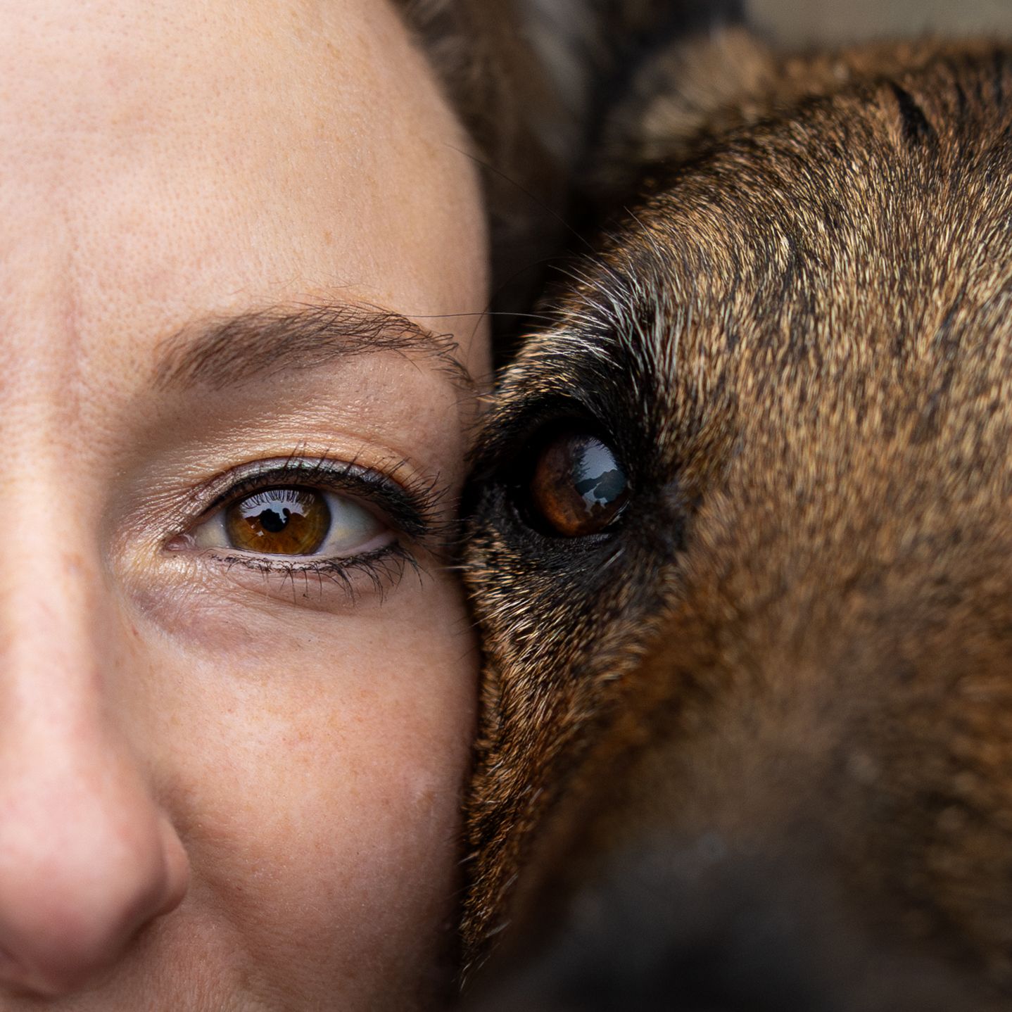 Close-up portrait of a woman and dog cheek to cheek showing matching brown eyes.