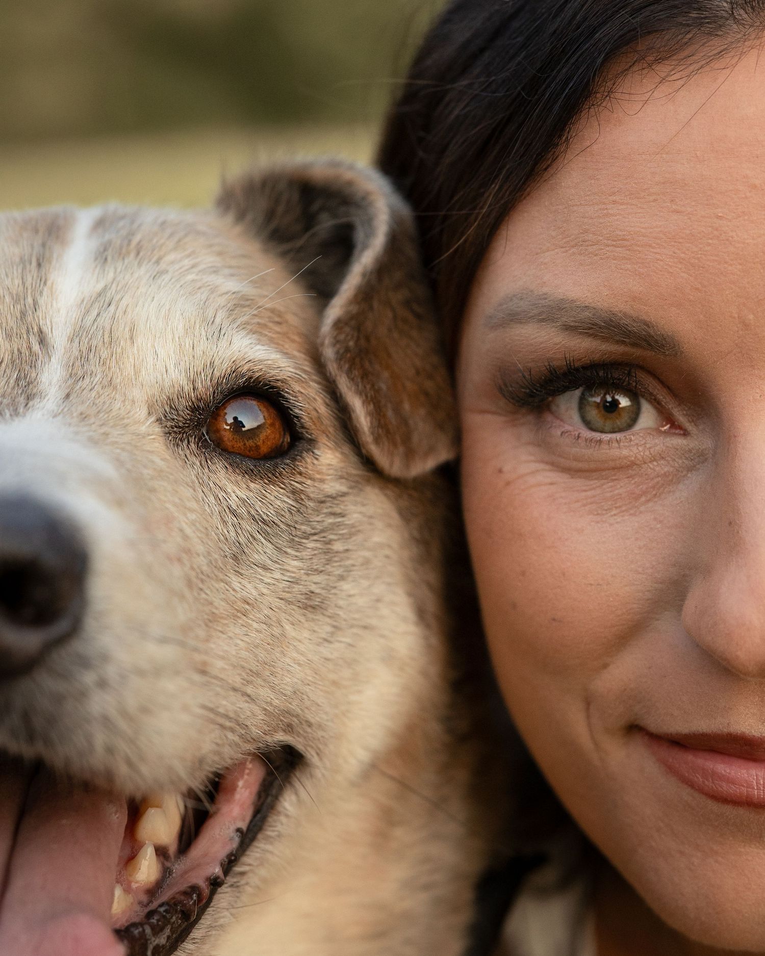 Close-up portrait of a woman with green eyes posing cheek-to-cheek with her mixed-breed dog.