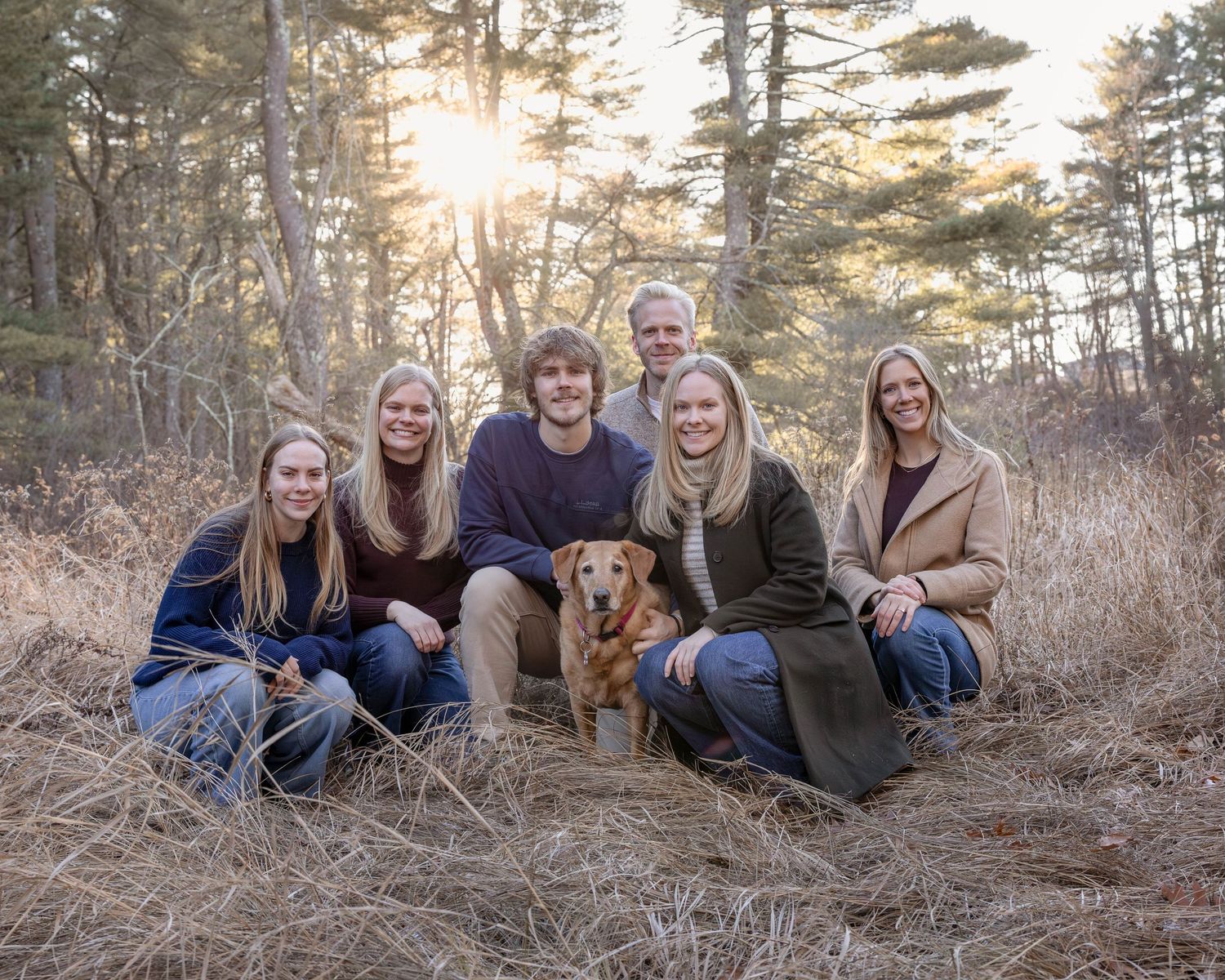 Family of six poses with golden retriever dog in autumn forest clearing at golden hour sunset.