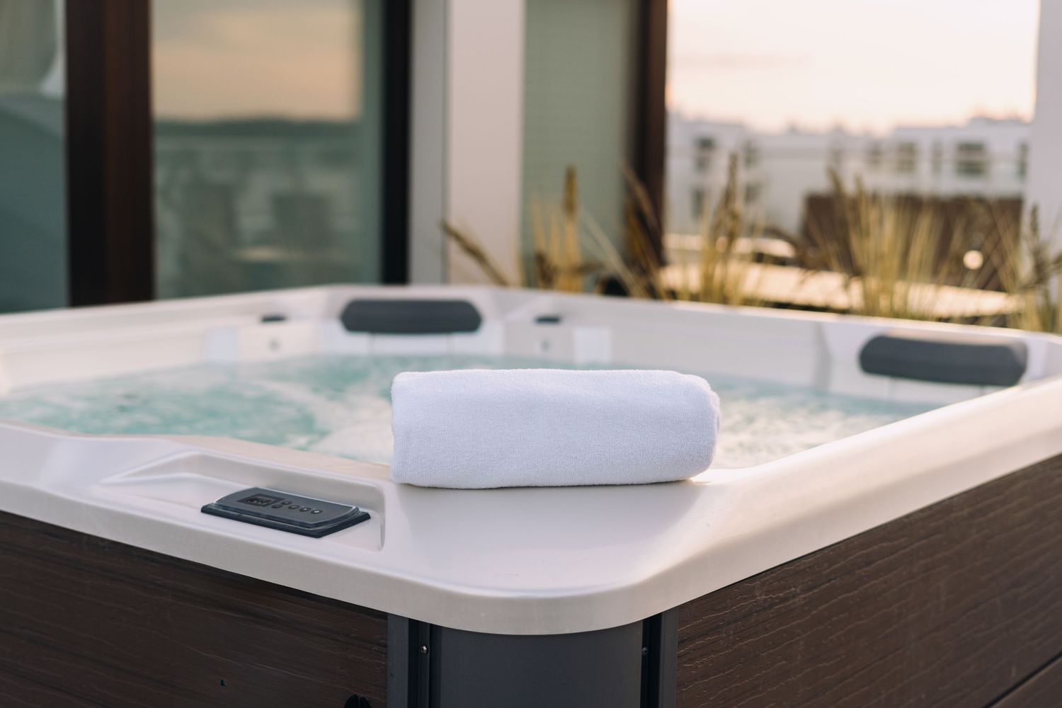 Rolled white towel resting on the edge of a hot tub overlooking a sunset view of nearby buildings.