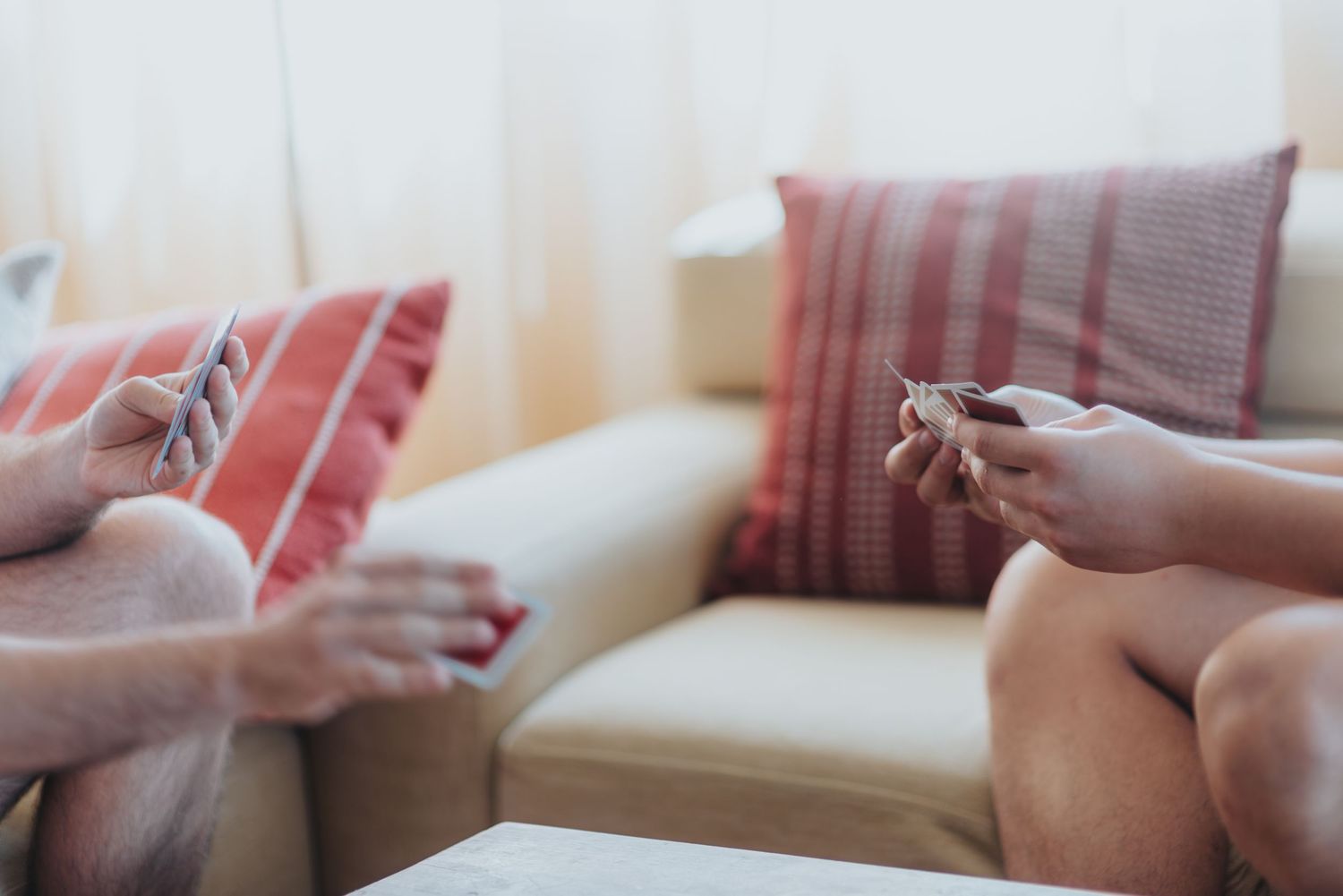 Two people sitting on a cream sofa with striped cushions, playing a card game in a relaxed living room.