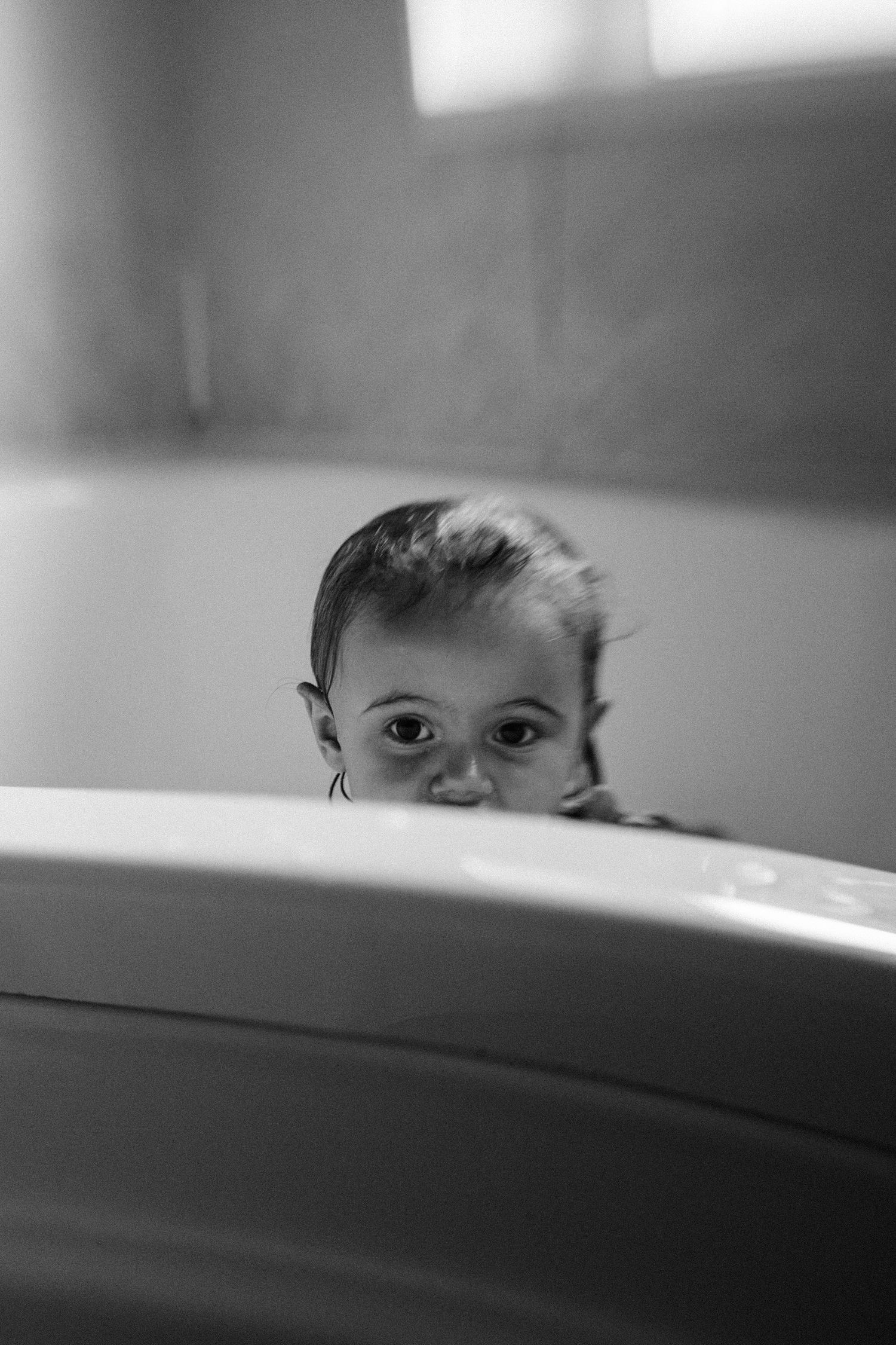 Black and white portrait of child peeking over bath