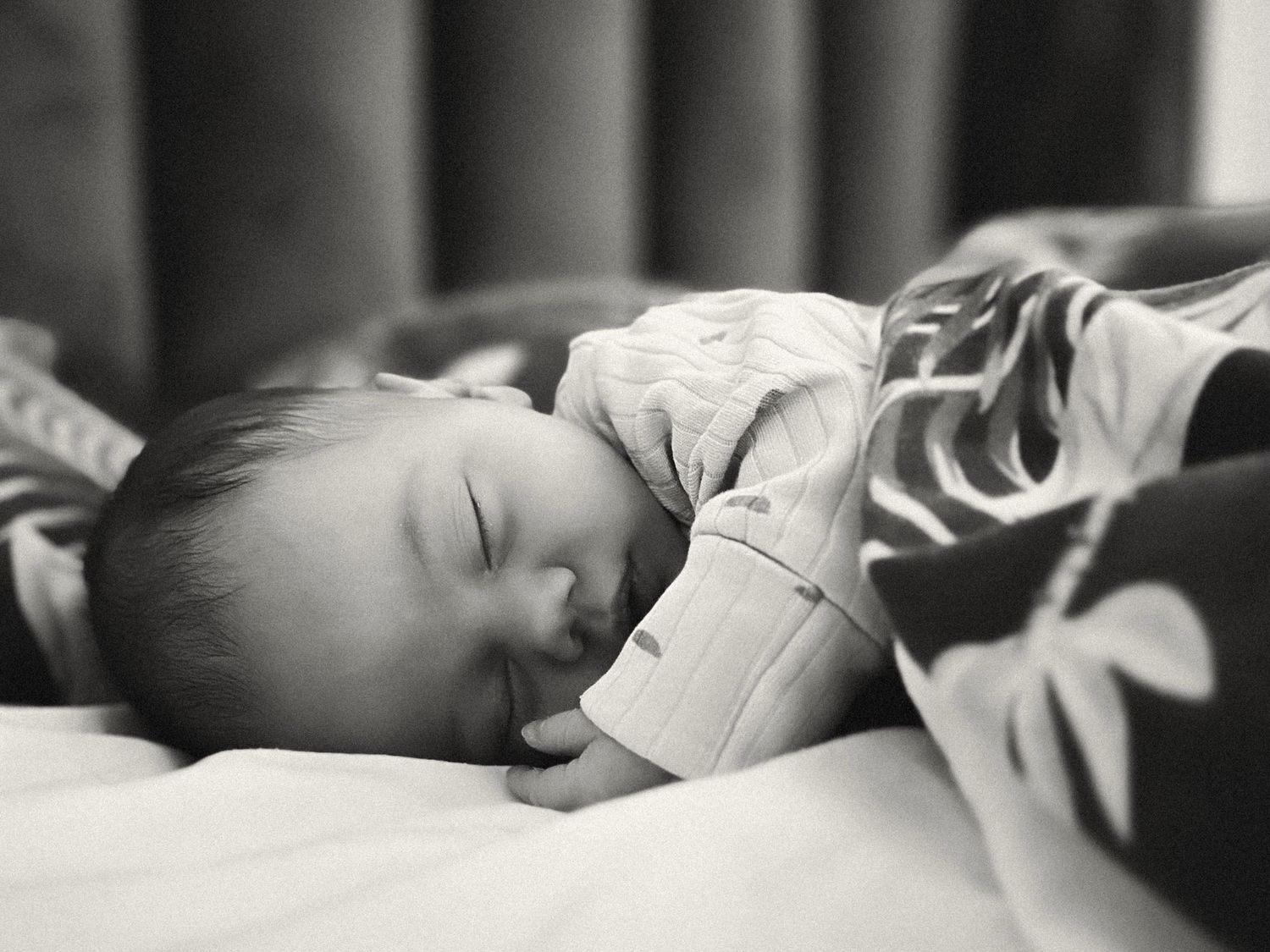 Black and white photo of a peaceful newborn baby sleeping soundly on a soft blanket.