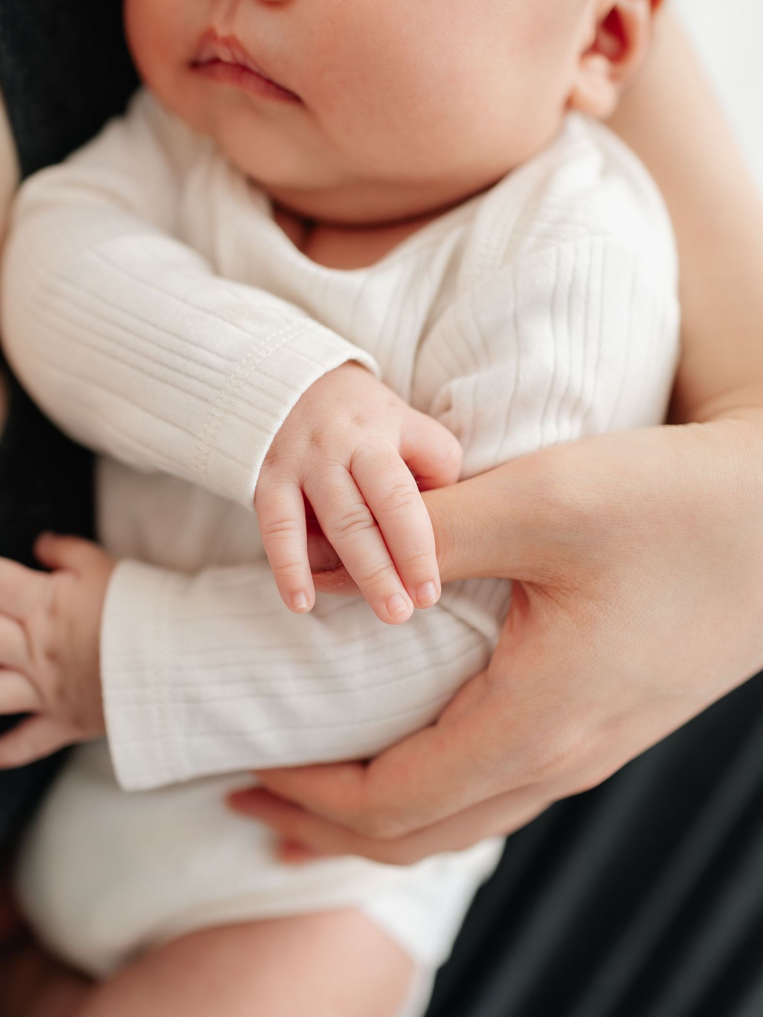 Close-up of a newborn baby in a white onesie with a parent's hand gently supporting them.