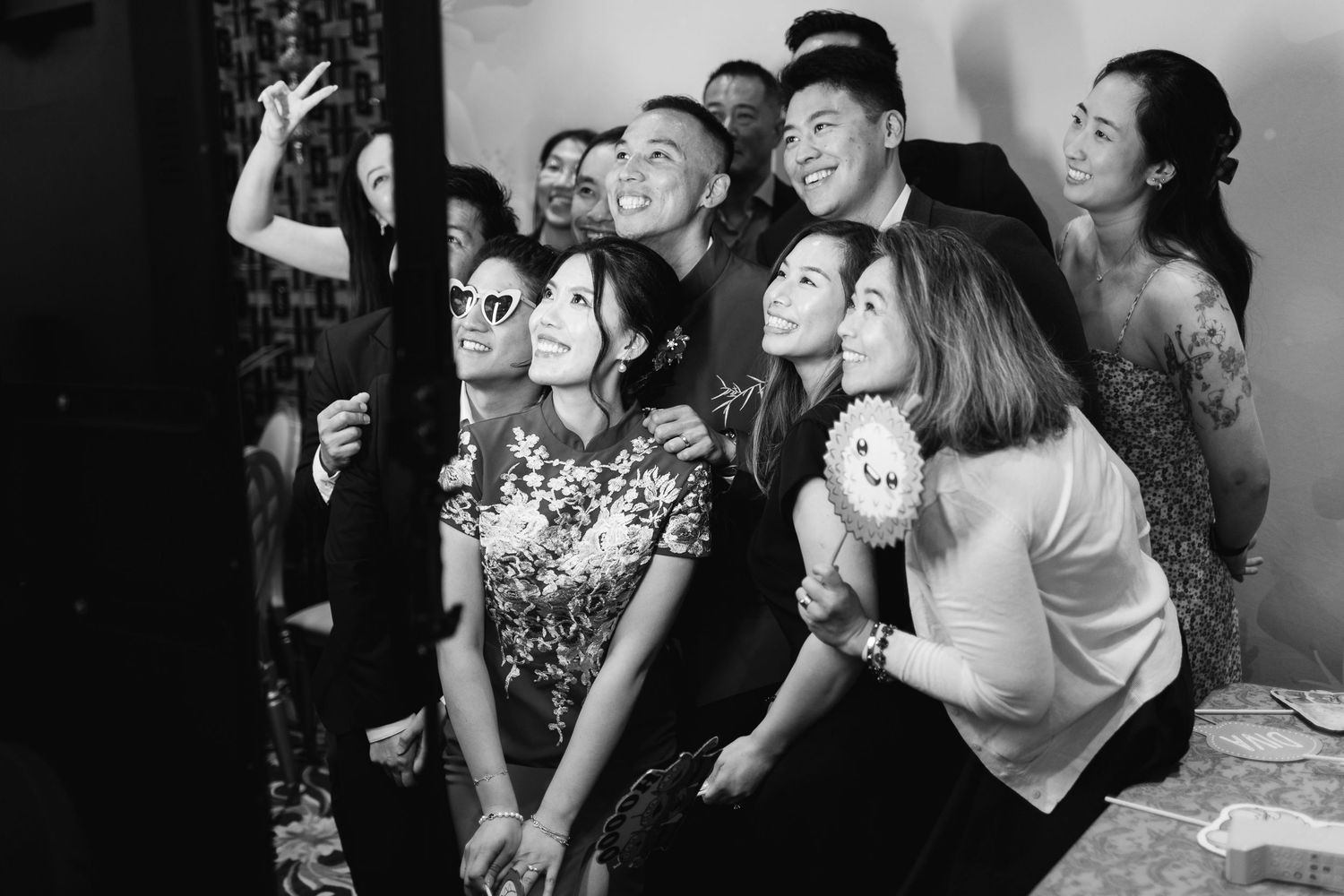 Black and white photo of a group of smiling friends in formal attire posing close together at a photo booth during a festive party.