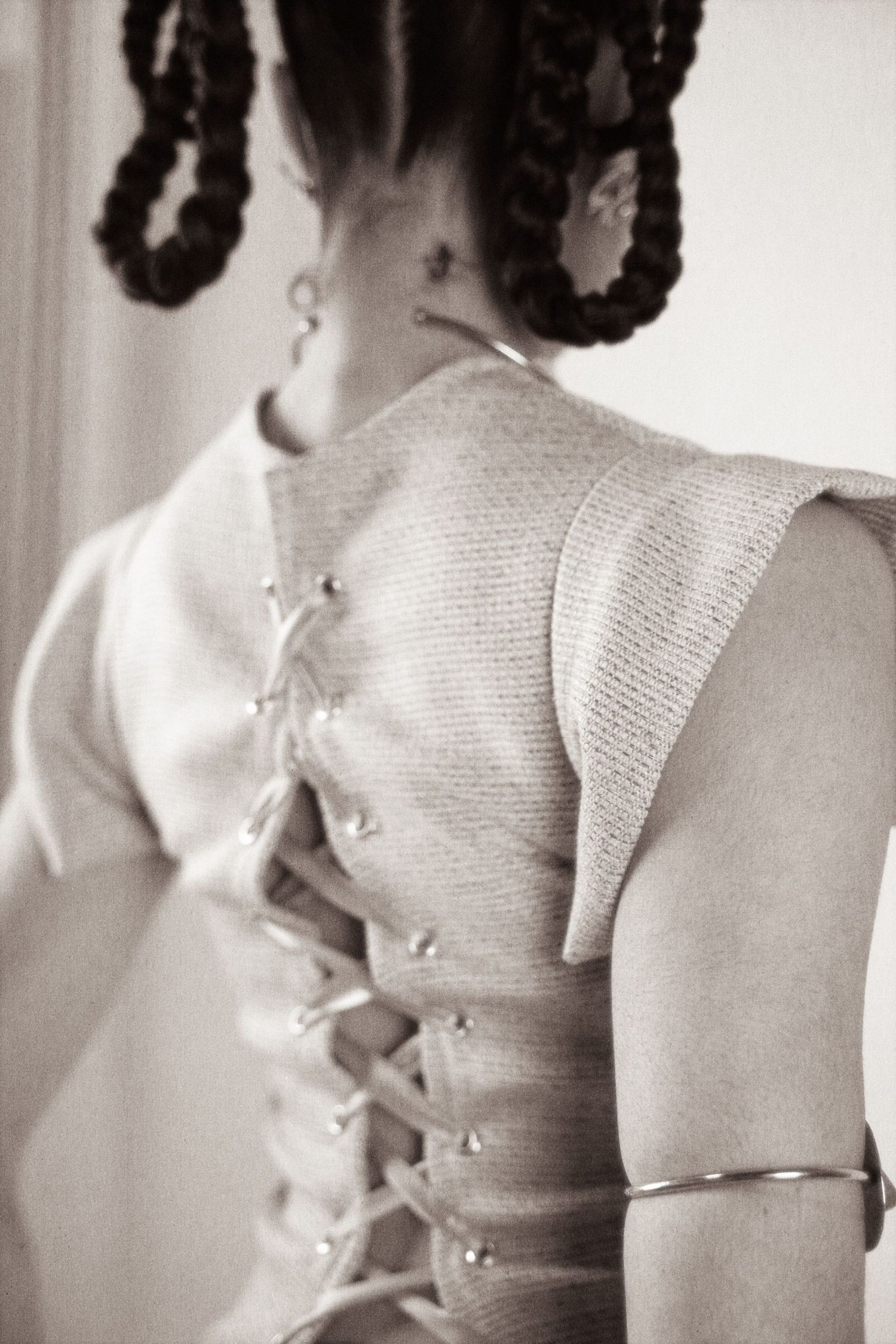 Black and white close-up of corset lace-back detail on a knit top with silver hardware and braided hair.