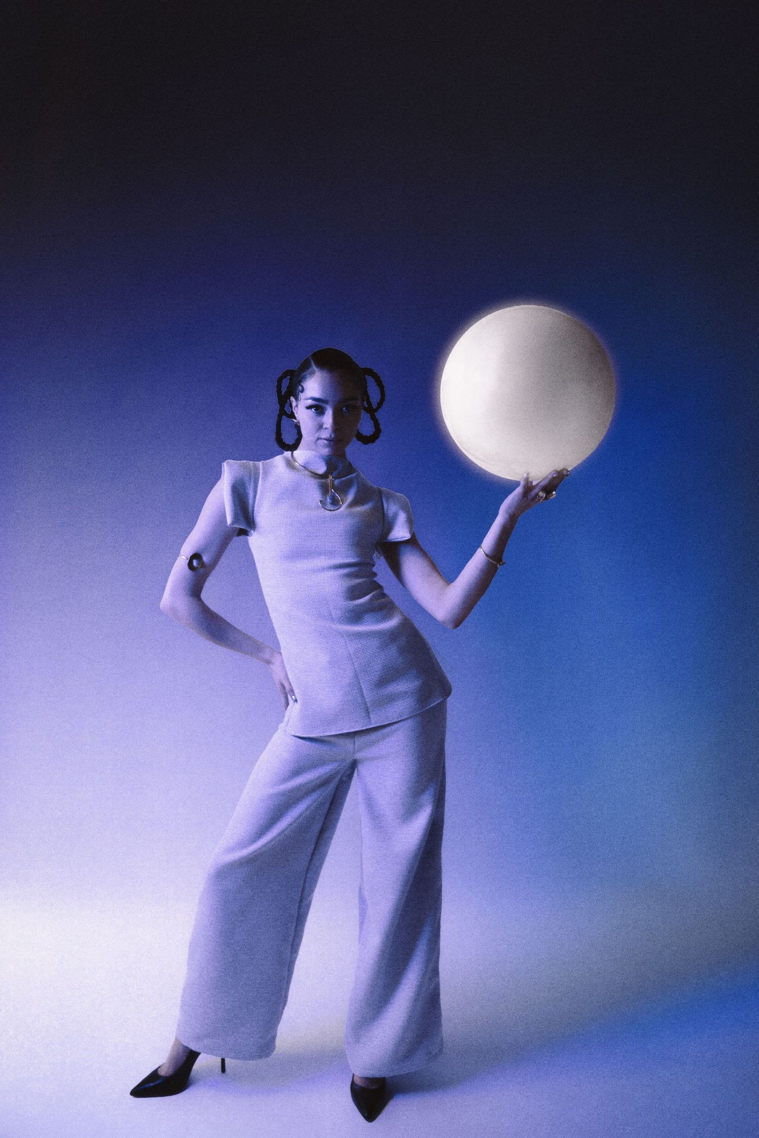 Woman in white wide-leg suit holding glowing orb on blue background.