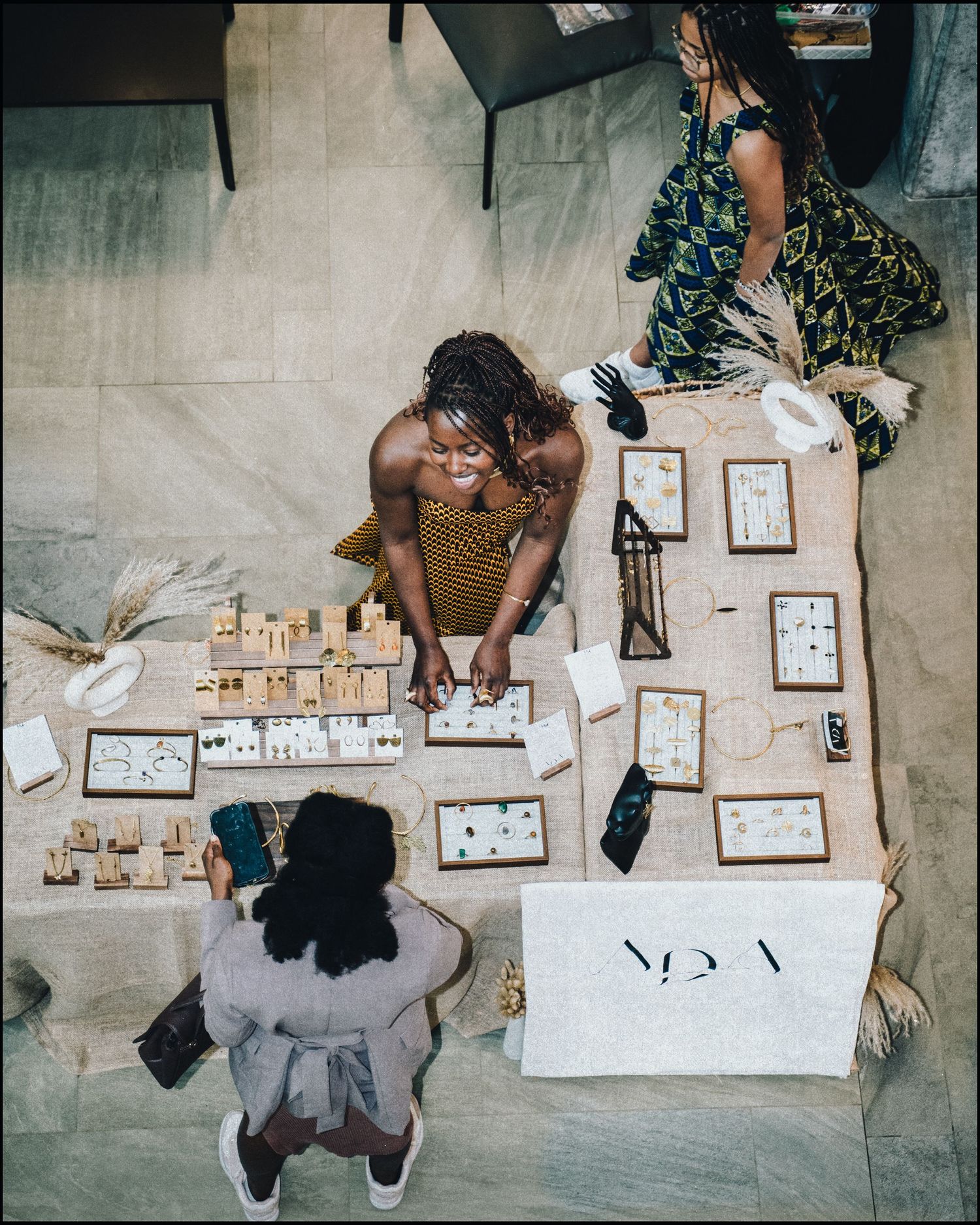 Overhead view of jewelry vendor displaying accessories at market table with customers.