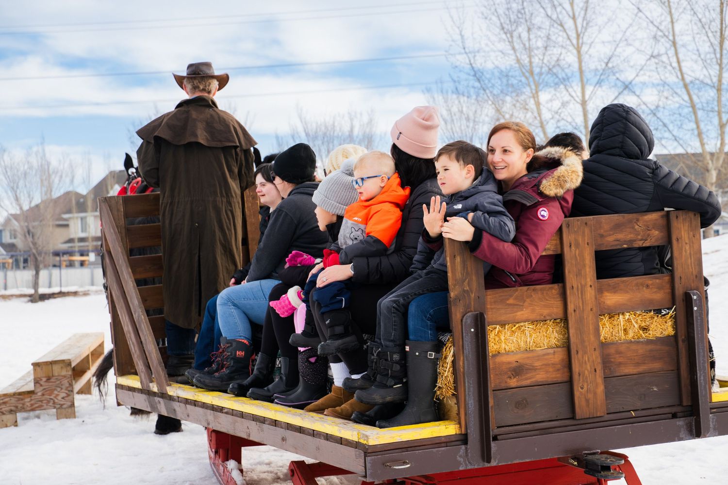 Family with children enjoying a horse-drawn sleigh ride through a snowy winter neighborhood.